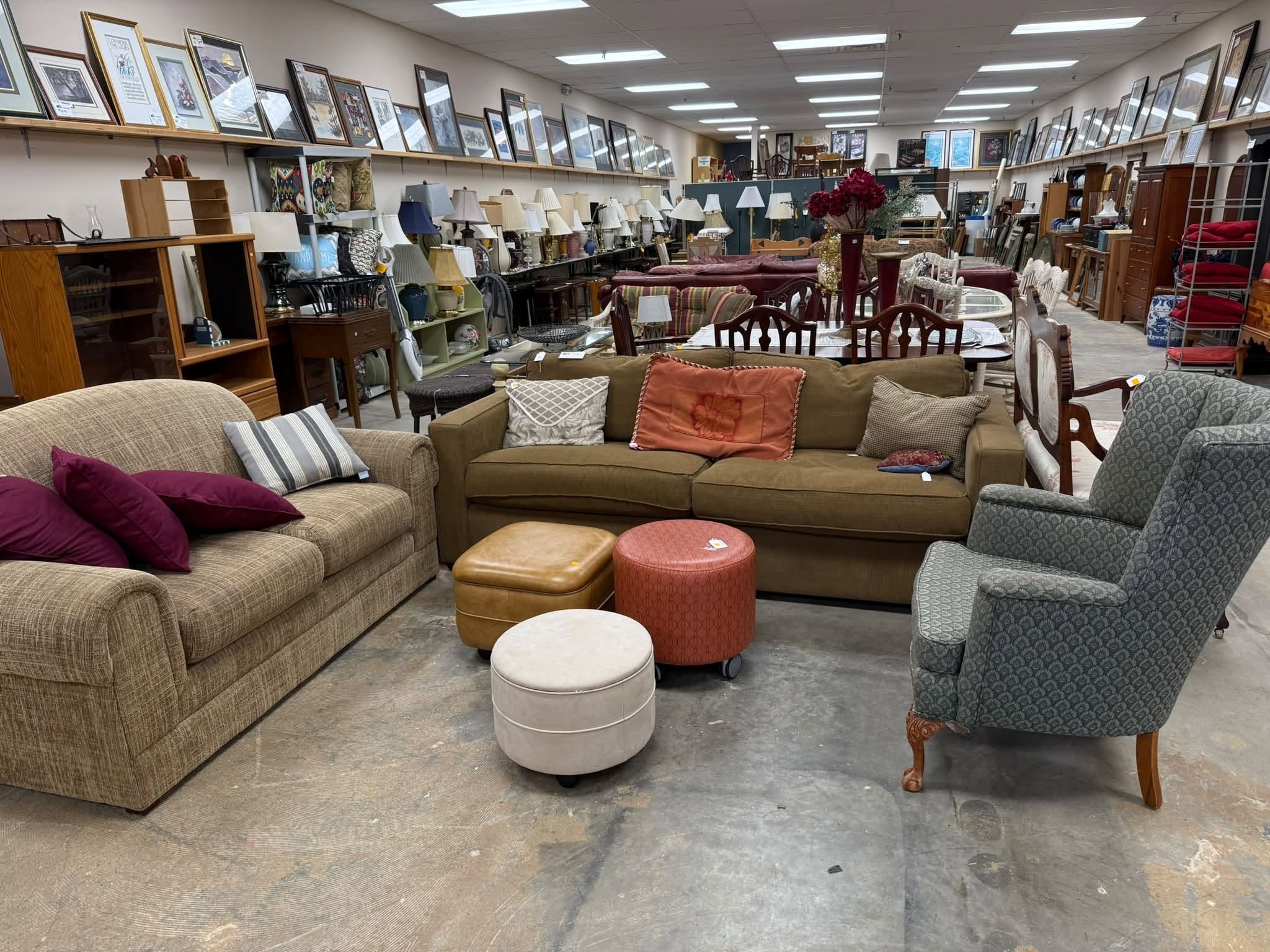 A furniture store displays various sofas, tables, and lamps with framed pictures on the wall behind.