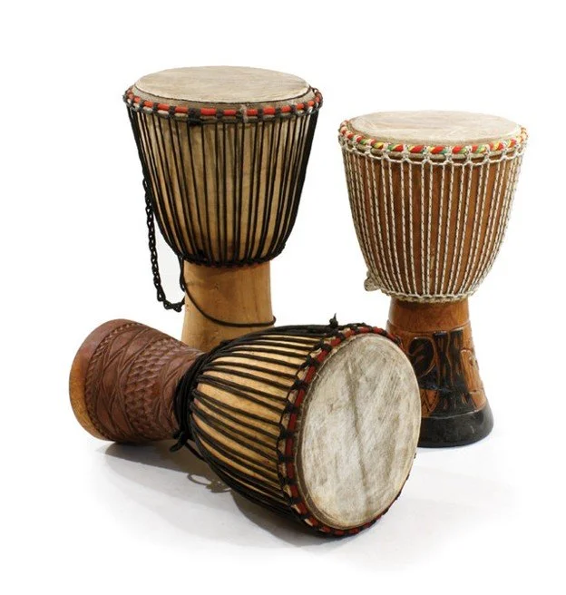 Set of three traditional African drums, two upright and one lying down, with wooden bodies and decorated drumheads.
