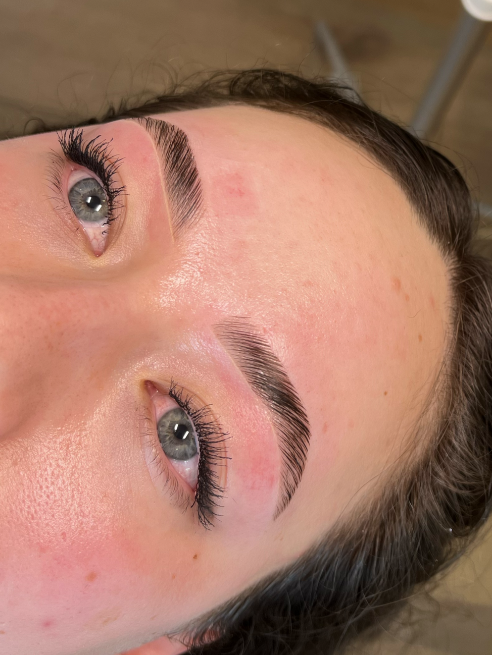 Close-up of a person's face showing freshly microbladed eyebrows and detailed eye makeup with mascara on the eyelashes.