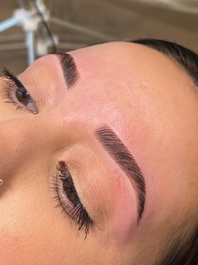 Close-up of a woman's face showing freshly done eyebrow microblading and makeup, with her eyes closed.