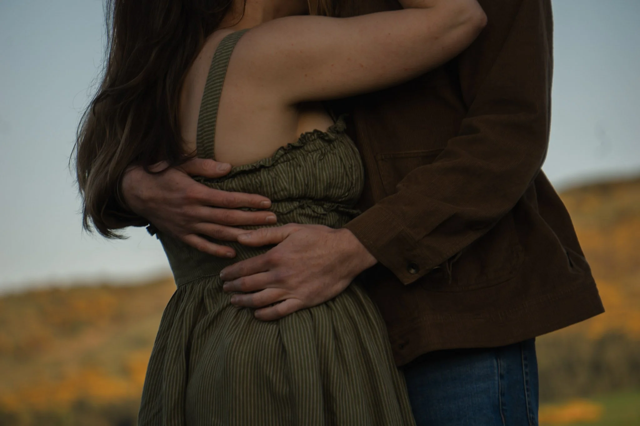 A close-up cinematic shot of a man's arms wrapped tightly around a woman wearing an earthy green dress during a photoshoot in Scotland.