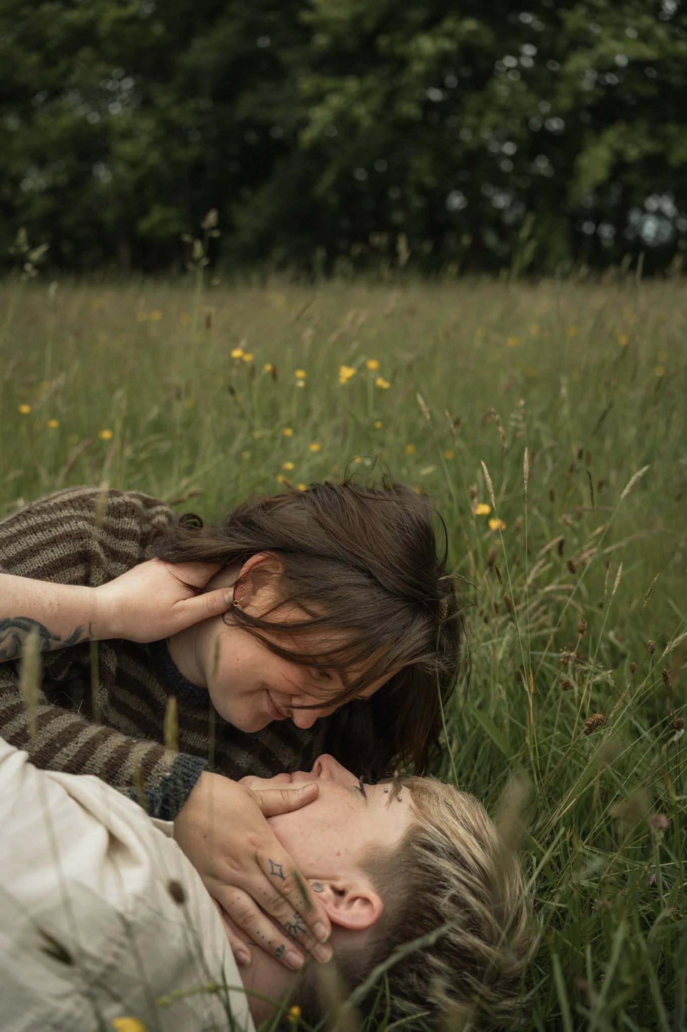 An intimate overhead perspective of a couple lying down together and laughing in thick, vibrant green grass.