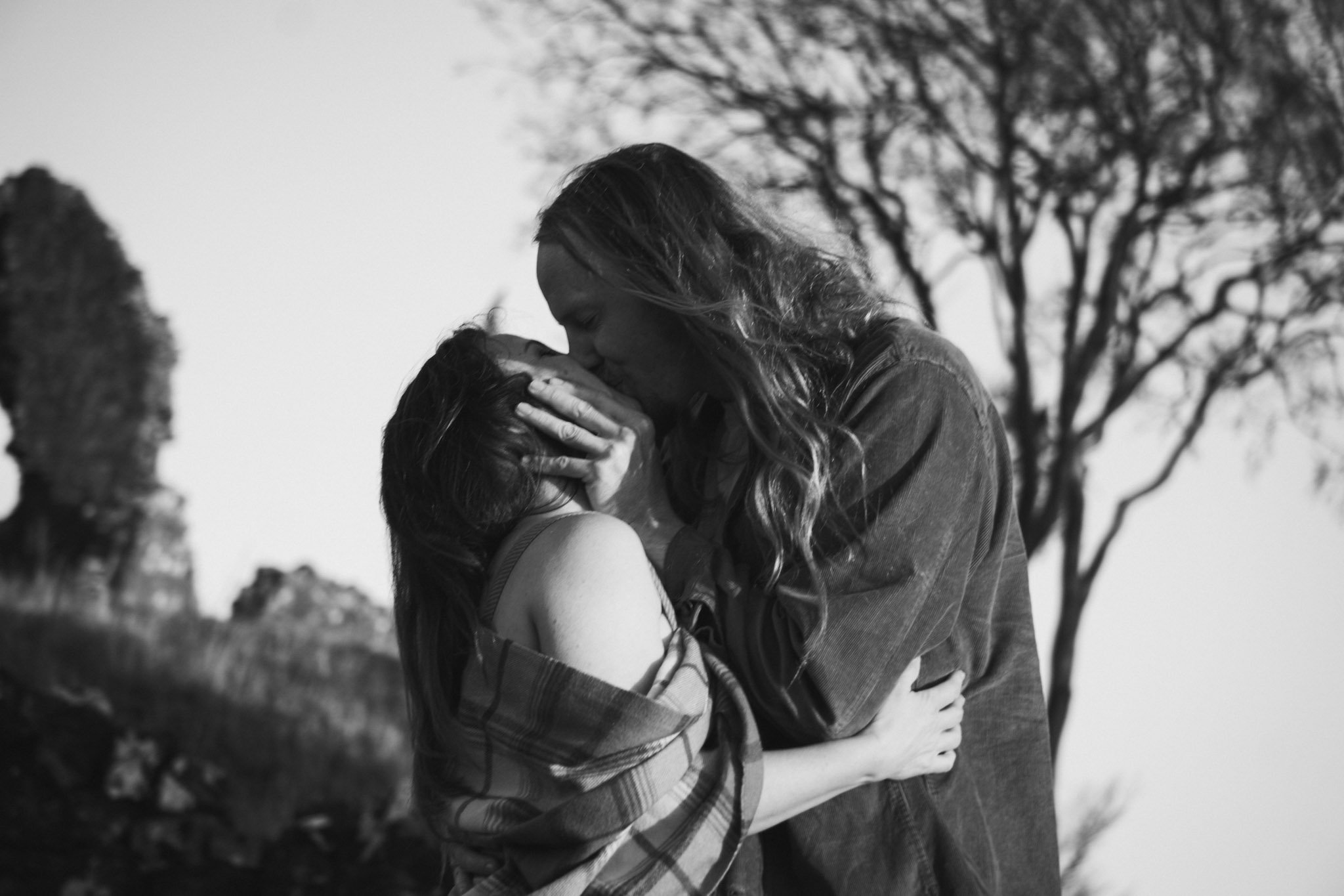 A moody black and white fine-art portrait of a long-haired couple embracing passionately outdoors by the ruins of a Scottish castle.