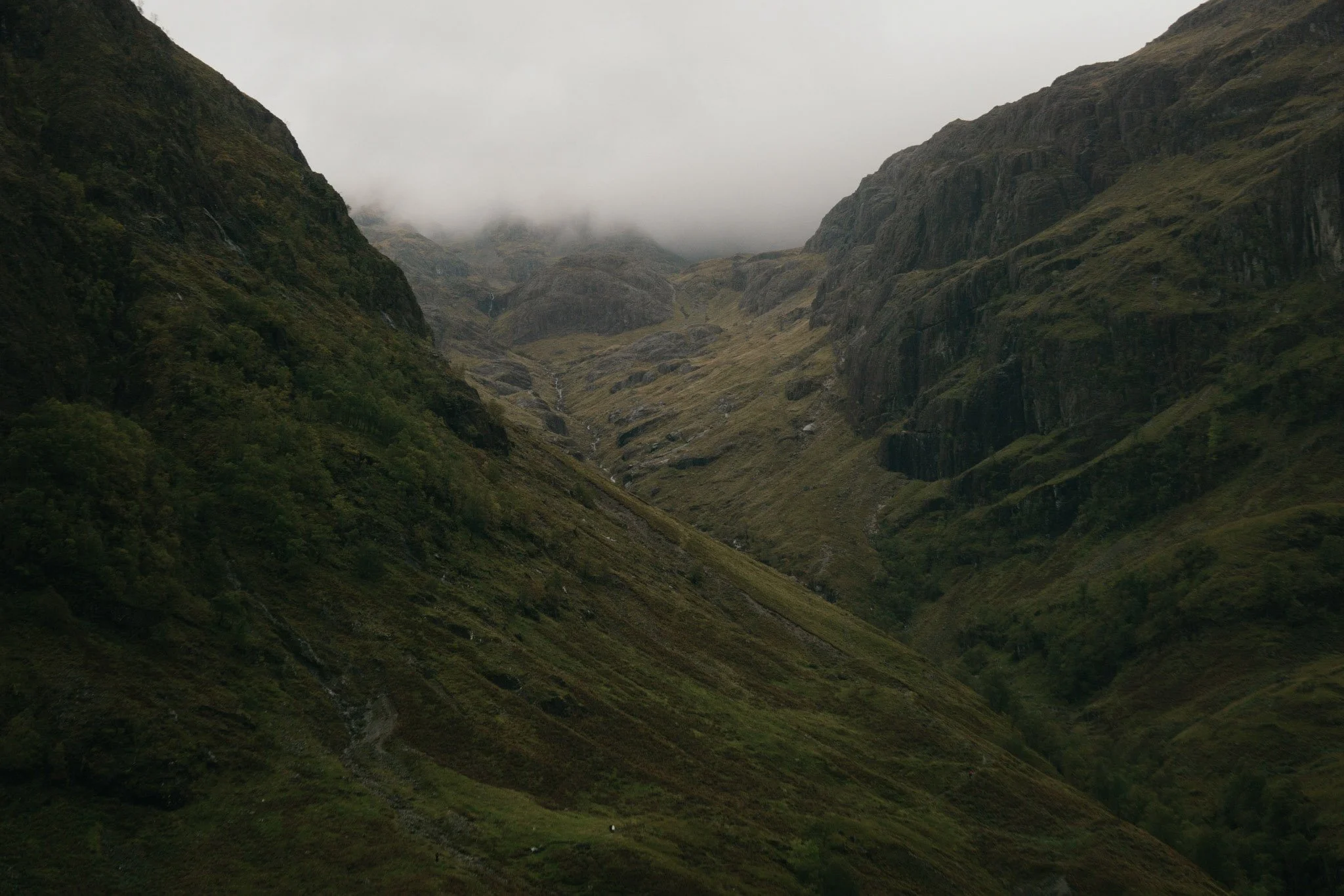 A breathtaking, moody landscape view looking down into the deep green mountain passes of a mist-covered Glencoe valley.