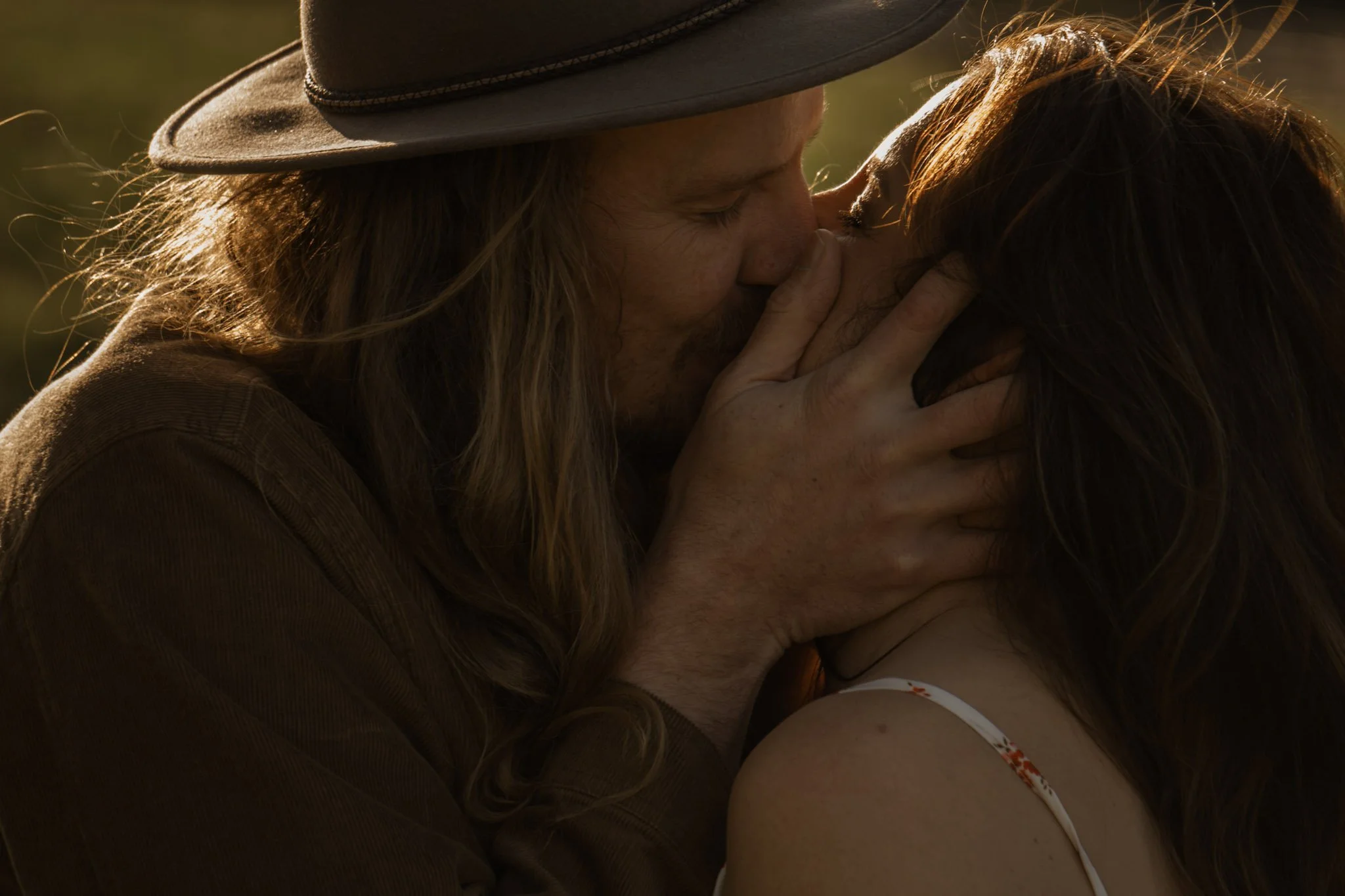 A close-up profile portrait of a romantic couple sharing a kiss during a warm golden hour sunset in the Scottish countryside.