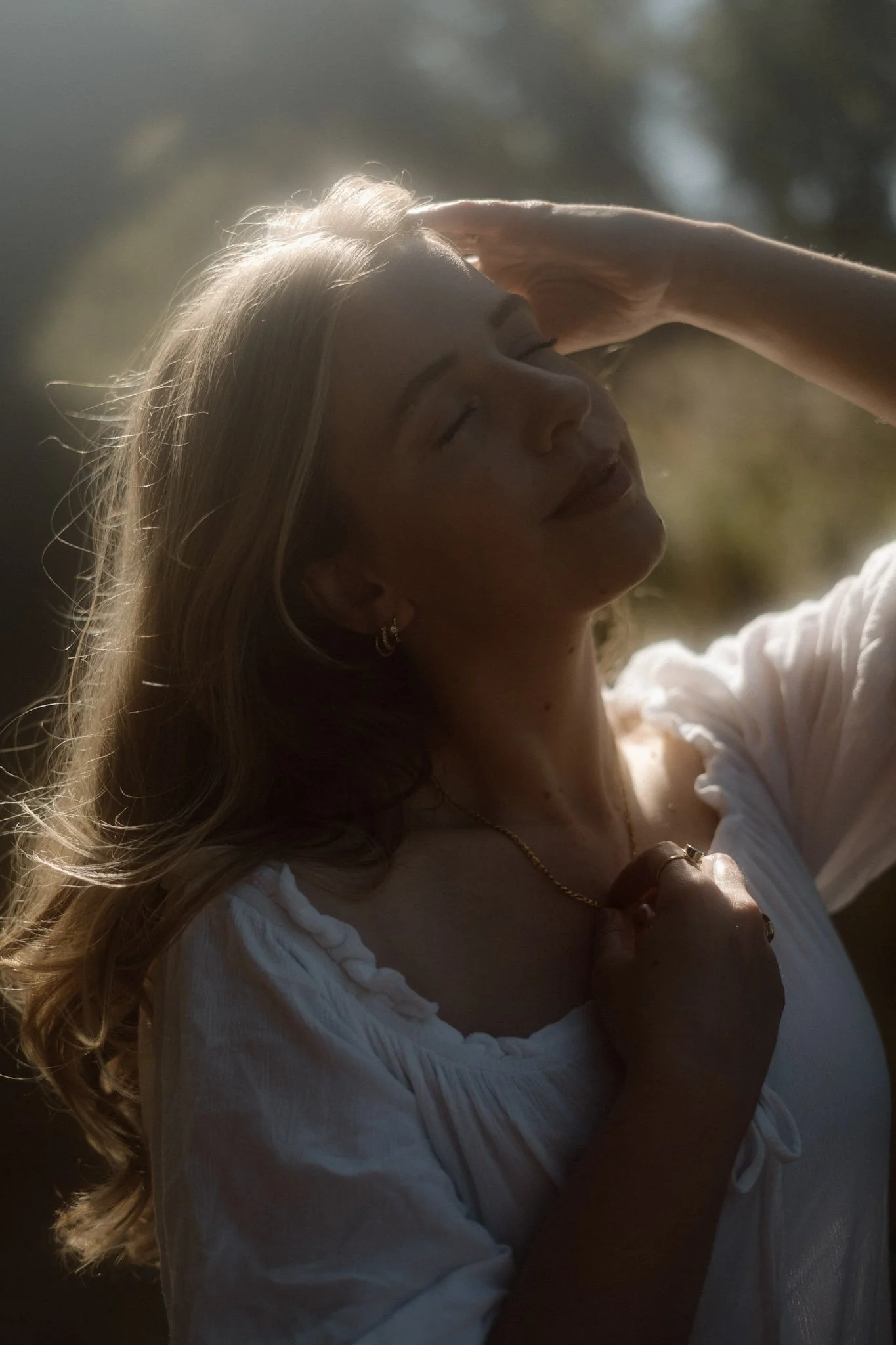 An ethereal, sun-drenched portrait of a woman looking upward as warm golden light catches her hair in a garden within Scotland.