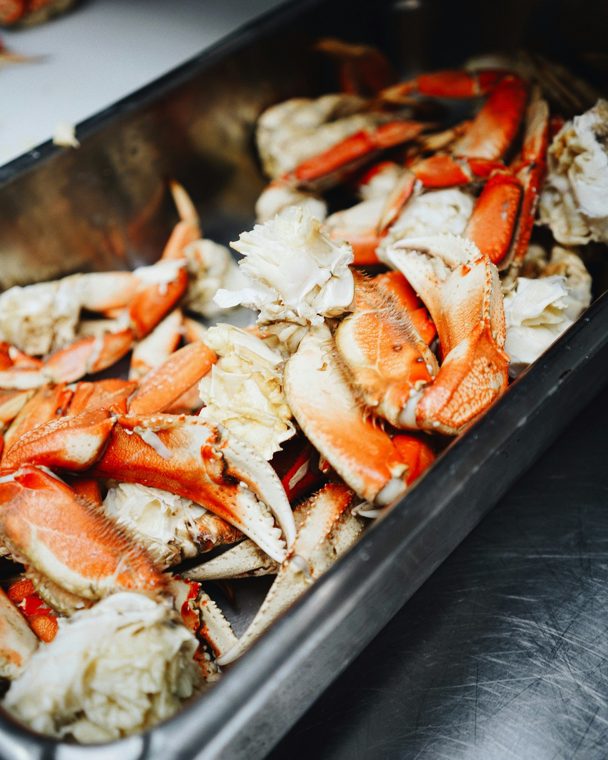 Crab legs and lobster meat in a metal container on a stainless steel surface.