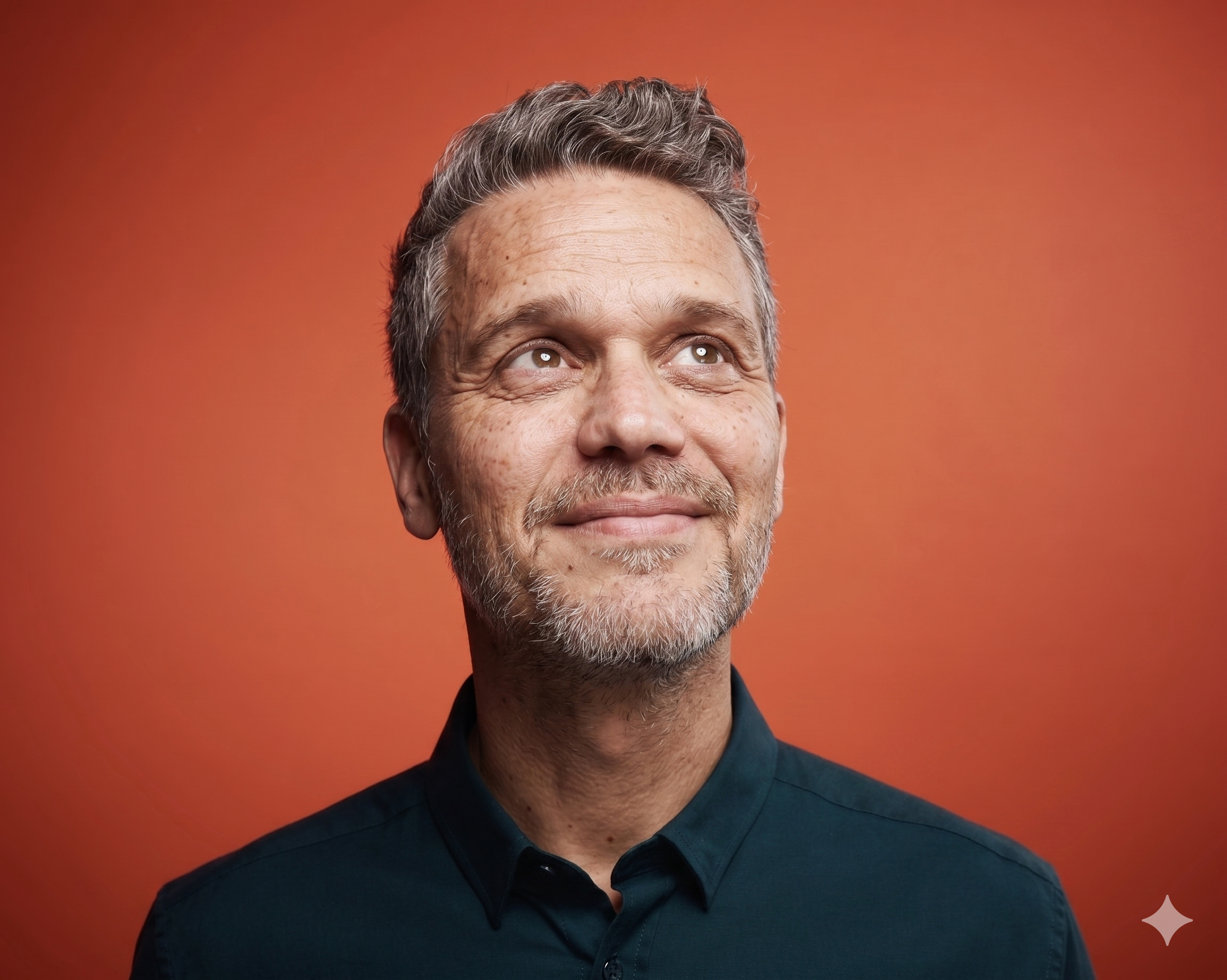 Portrait eines lächelnden Mannes mittleren Alters mit grauem Haar und Bart vor einem orangefarbenen Hintergrund. Er denkt darüber nach, wie Künstliche Intelligenz Unternehmen hilft.