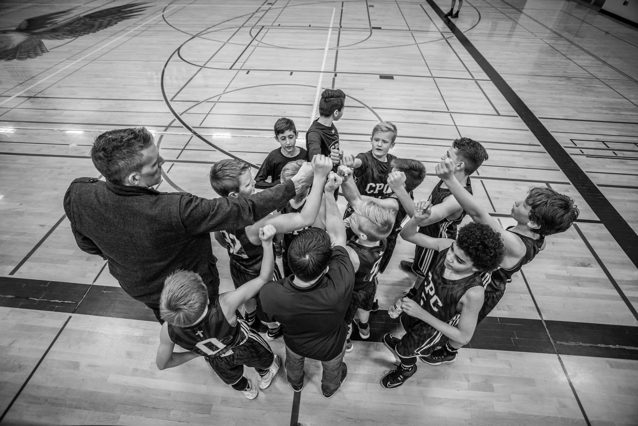 A group of young basketball players in jerseys huddled in a circle, fist-bumping each other on a basketball court.
