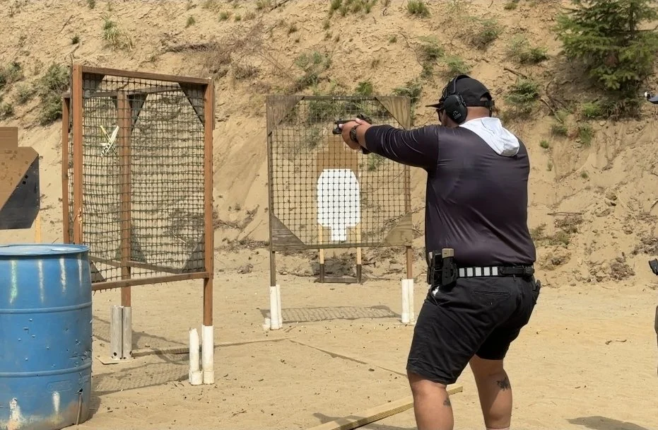 A person practicing shooting at an outdoor shooting range with a paper target in the background.