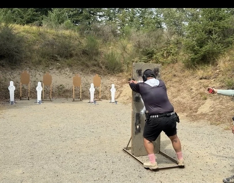 A person shooting at a target with a firearm at an outdoor shooting range, with multiple paper targets set up in the background.