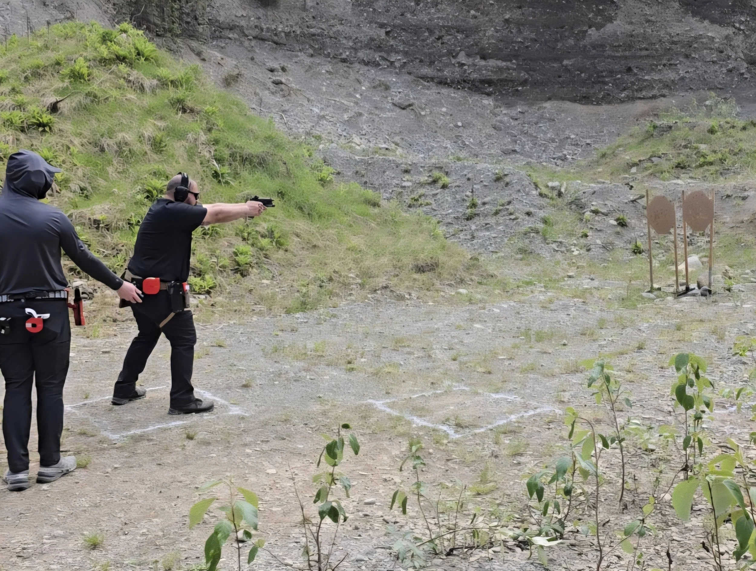 Two men at a shooting range aiming at targets on a rocky hillside. One is firing a handgun, while the other is observing.