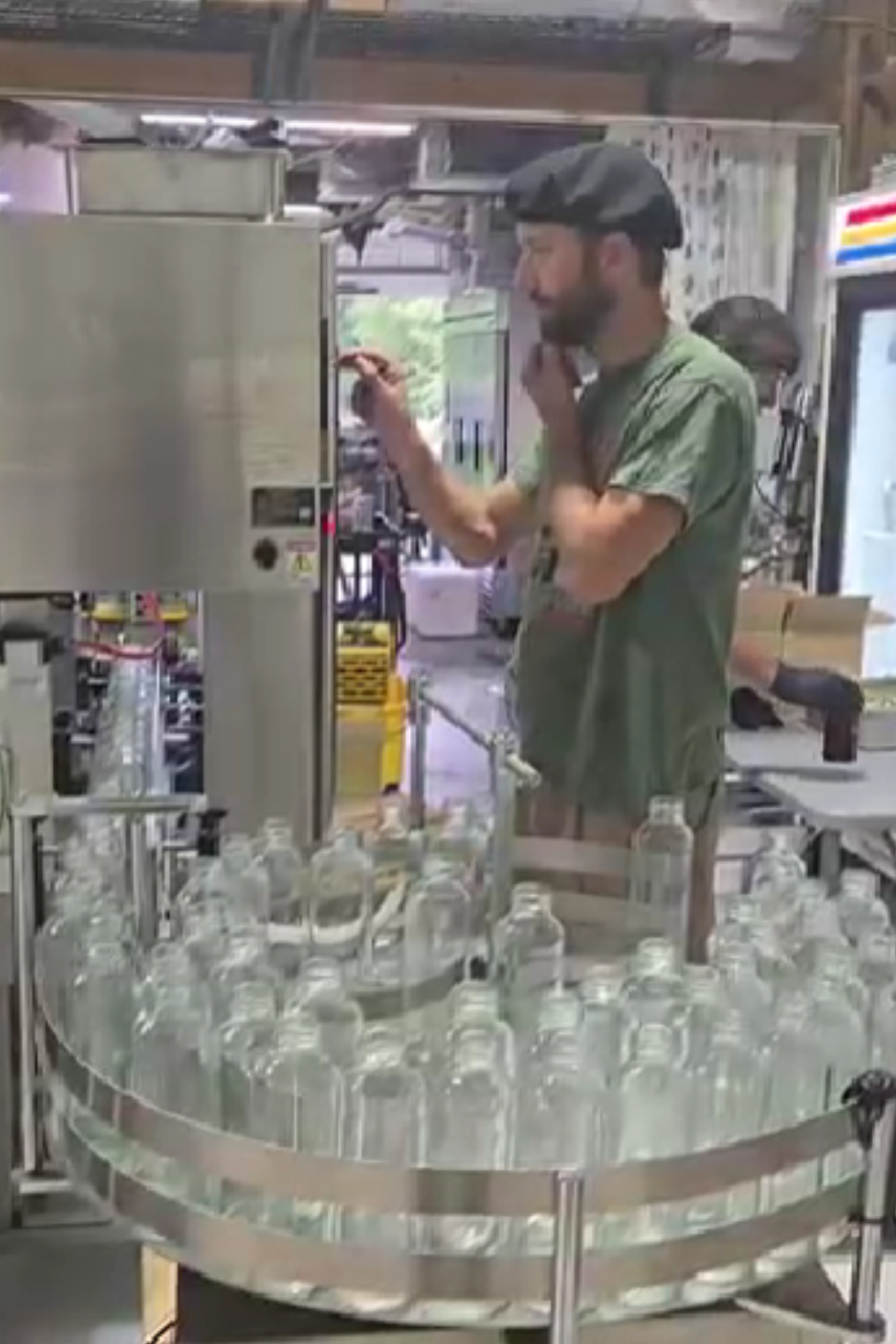 Operator monitoring an automated bottling line in a commercial processing facility as glass bottles are prepared for filling, packaging, and distribution of value-added agricultural products.