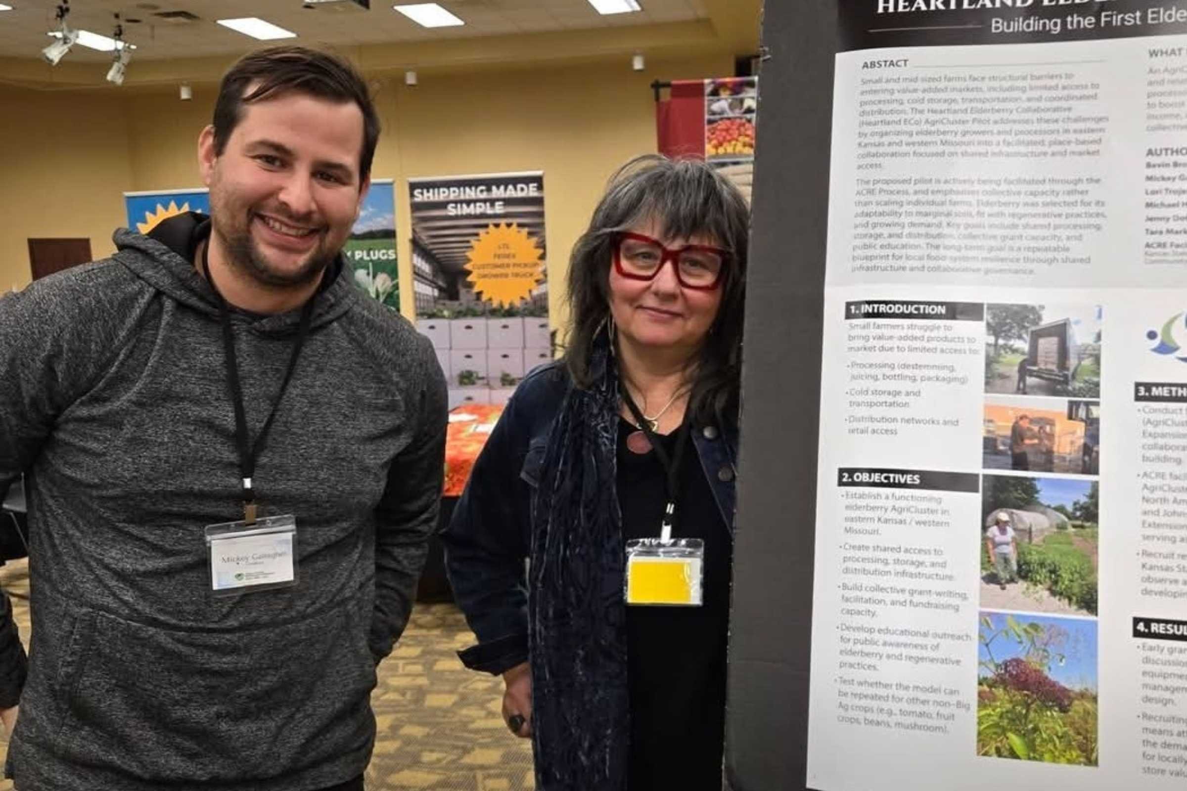 Two attendees stand beside a research poster about the Heartland American Elderberry Collaborative (HAECo) at the American Elderberry Conference.