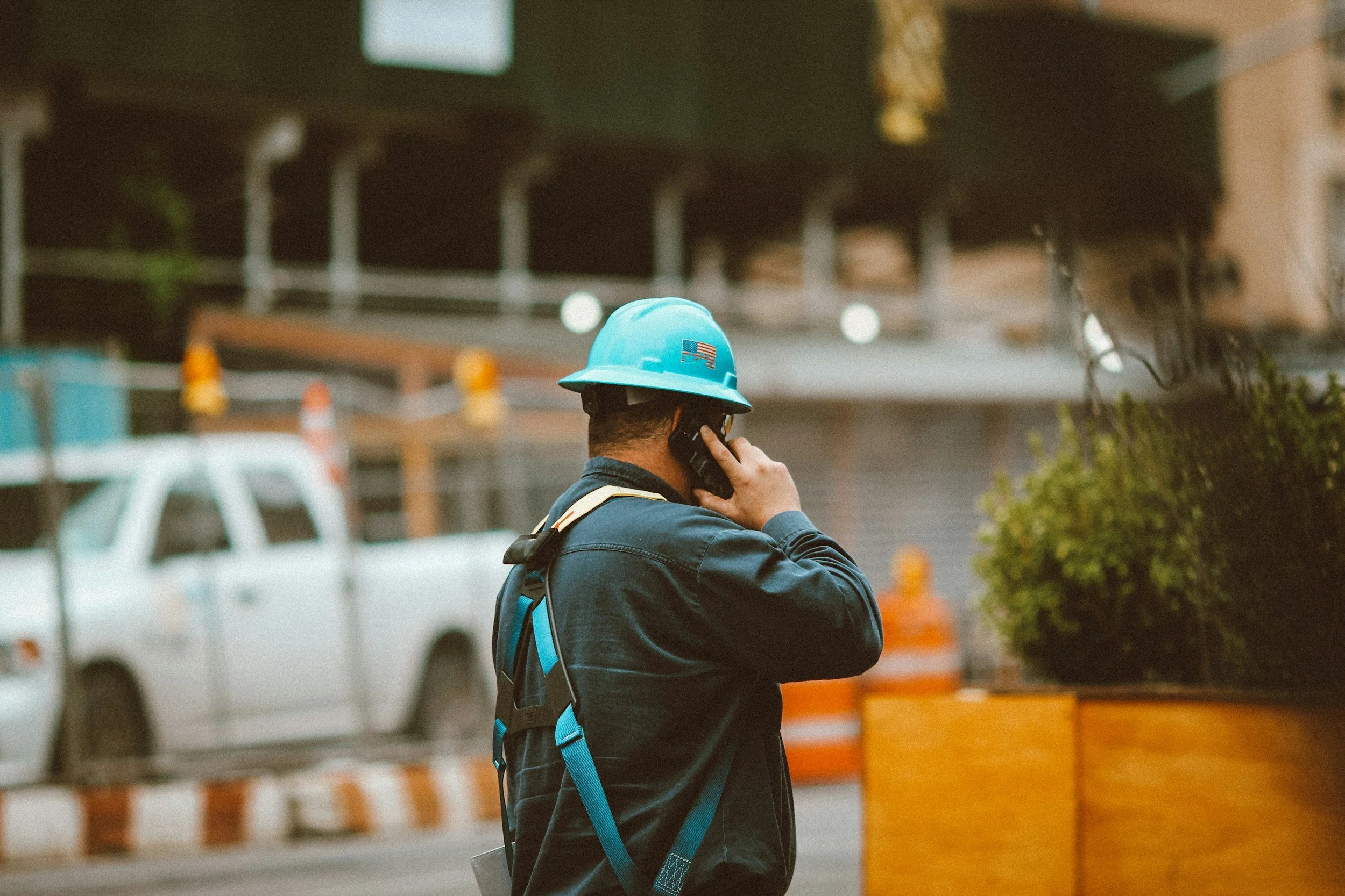 Contractor wearing a blue safety helmet talking on a cellphone near construction site barriers.