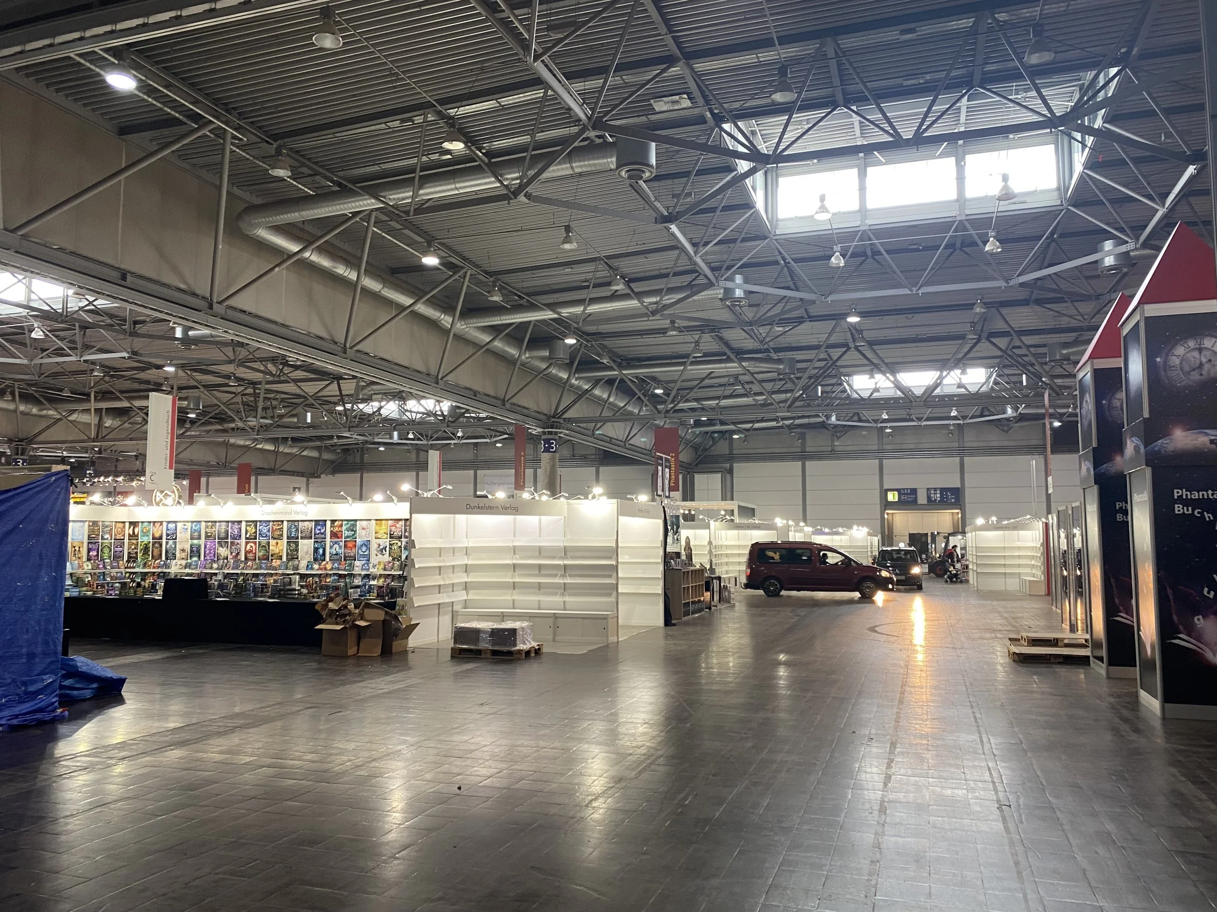 Innenansicht eines großen, leeren Messe- oder Hallengebäudes mit einem metalldach und einigen Regalen sowie einem geparkten Fahrzeug.