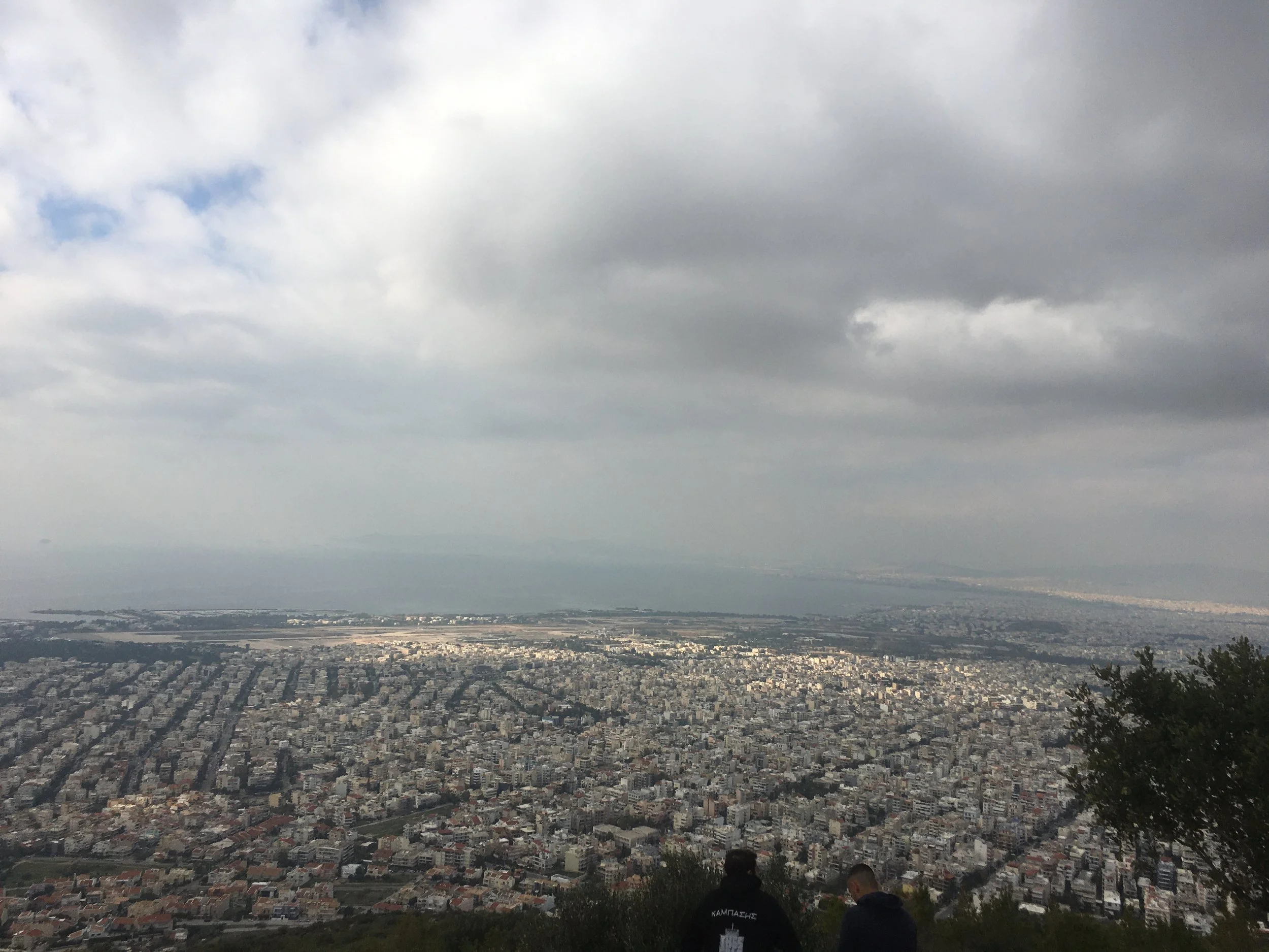 Blick auf eine große Stadt mit Wohnhäusern, in der Ferne das Meer und der Himmel mit dichten Wolken.