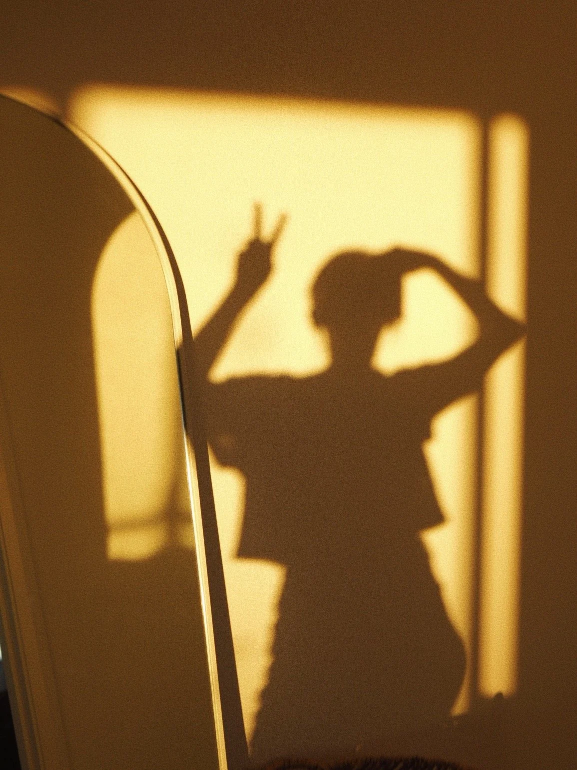 Shadow of a person making a peace sign with their fingers, projected on a wall with warm lighting.