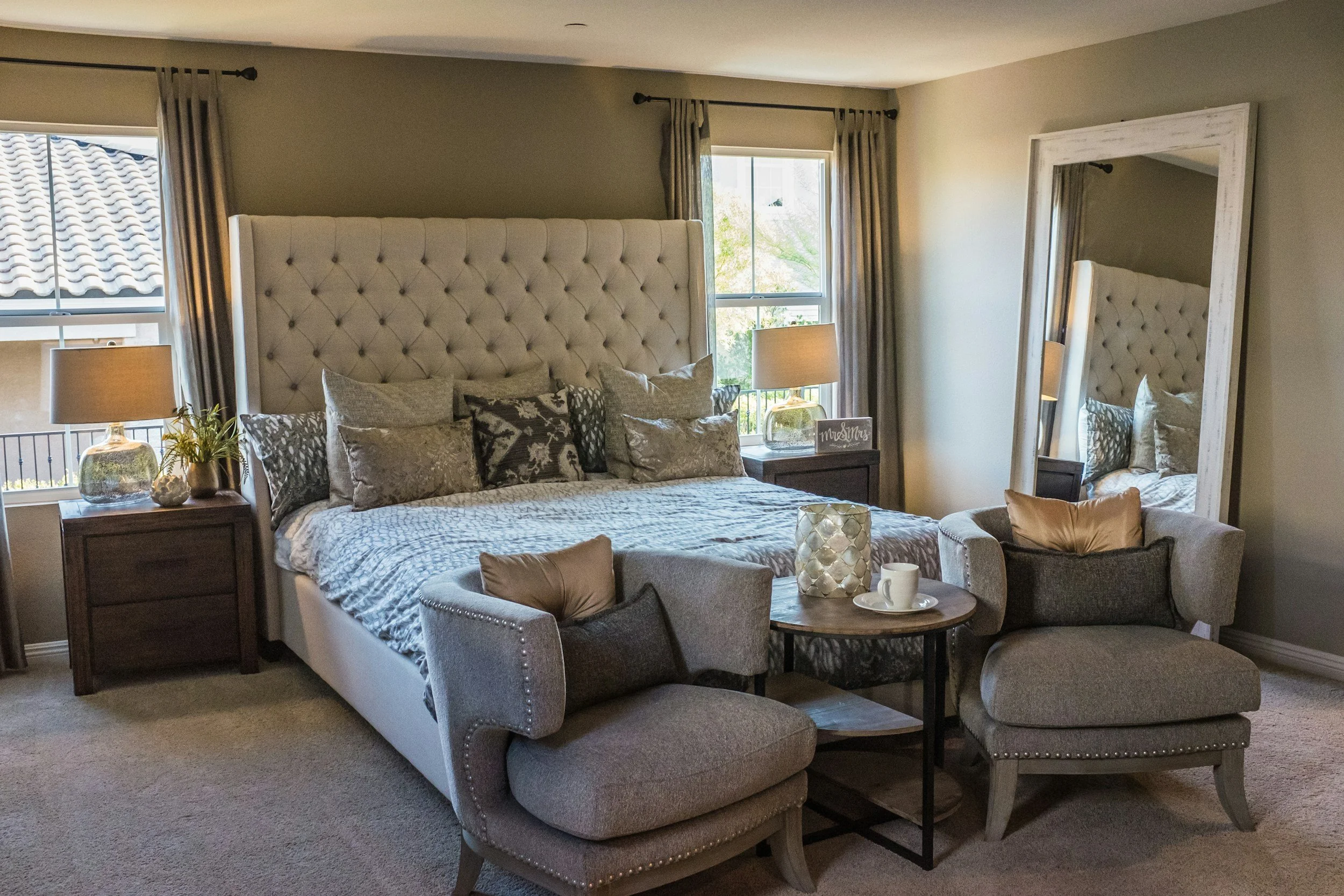 Blueprint Elite Realty — Georgia's luxury boutique real estate brokerage —Staged modern luxe bedroom with a large bed having a tufted beige headboard, surrounded by pillows with a neutral color palette. 