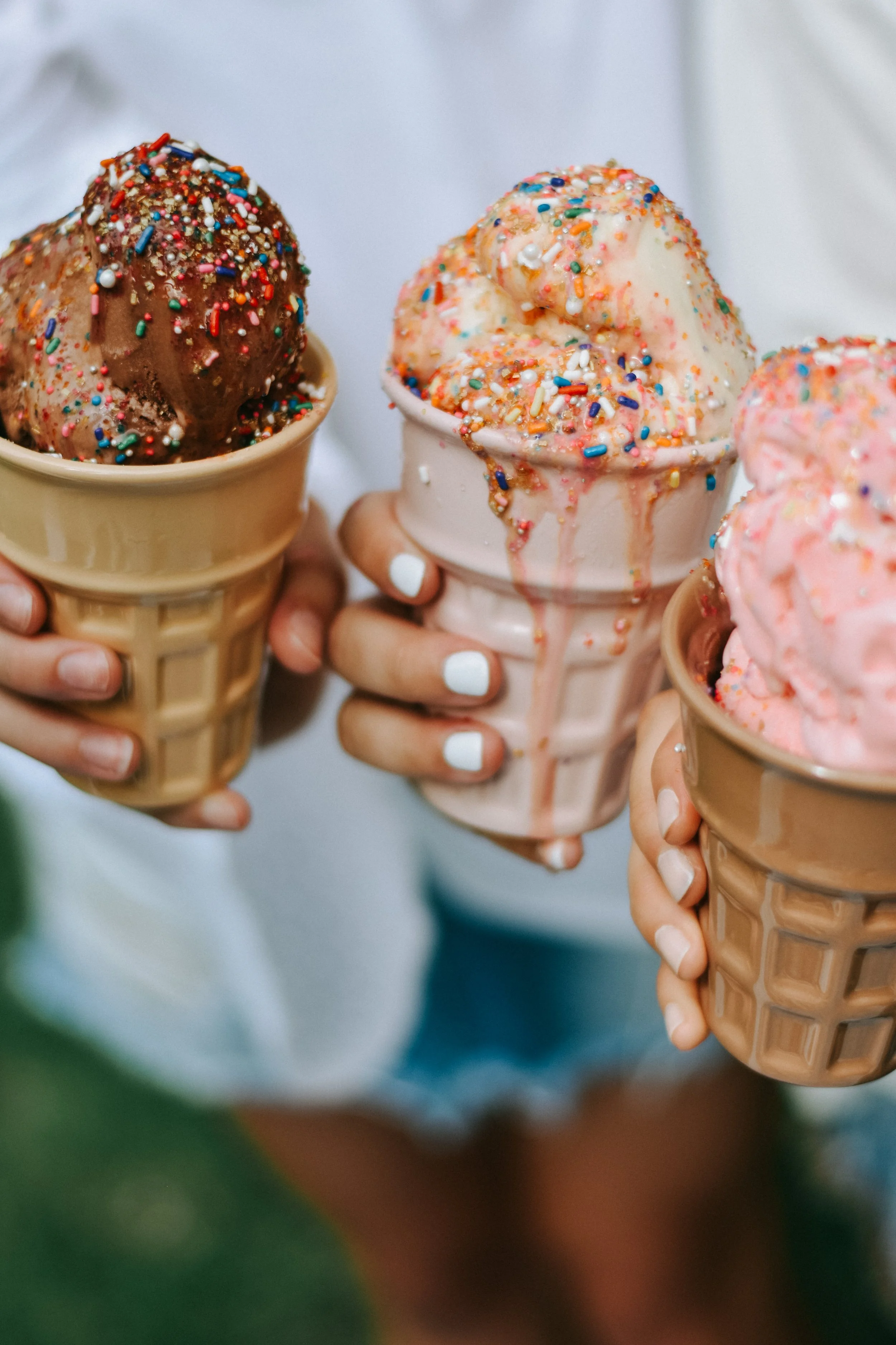 Three children holding ice cream cones with sprinkles, with a close-up view of their hands and ice cream cones.