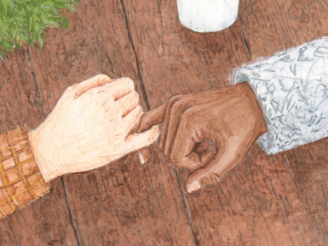 Close-up of two hands, one light-skinned and one dark-skinned, touching fingers on a wooden surface, with a white cup and a cloth nearby.