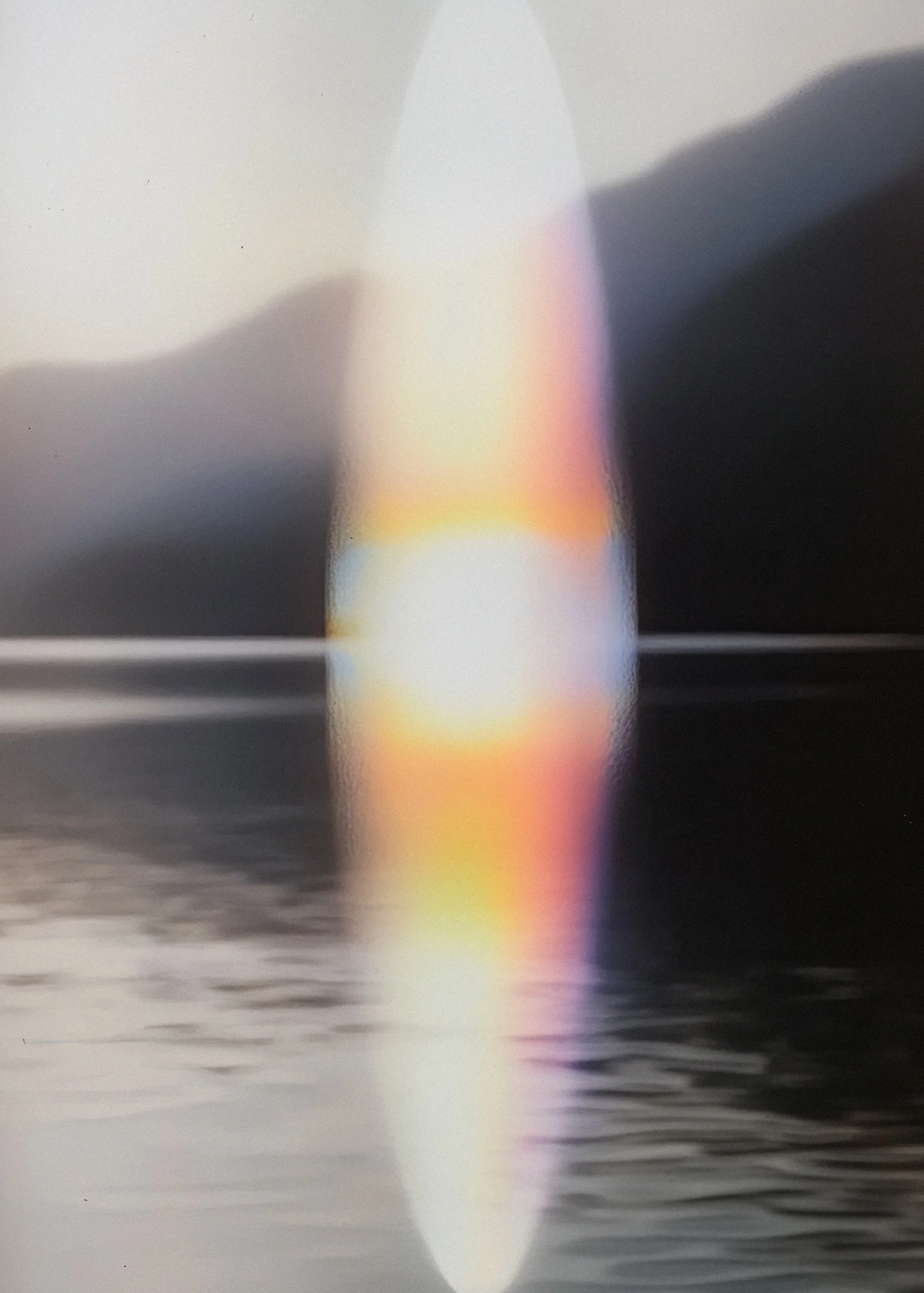 A blurred photo of a rainbow reflecting on water with dark and light areas.
