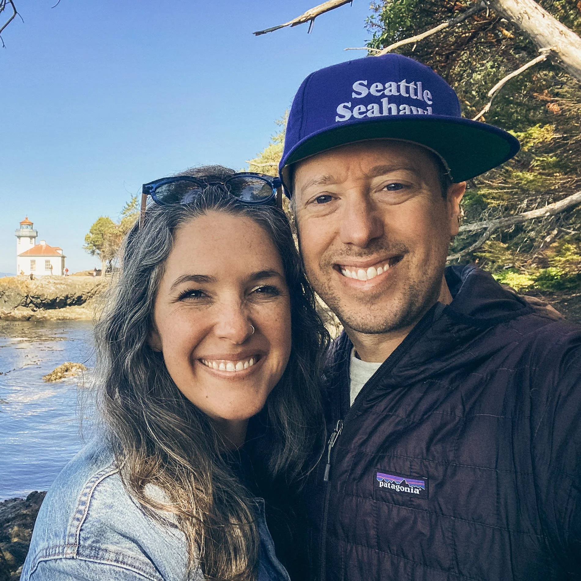 Nichelle and John Keatley, founders of ADMRL, smiling outdoors near a Pacific Northwest lighthouse and waterway