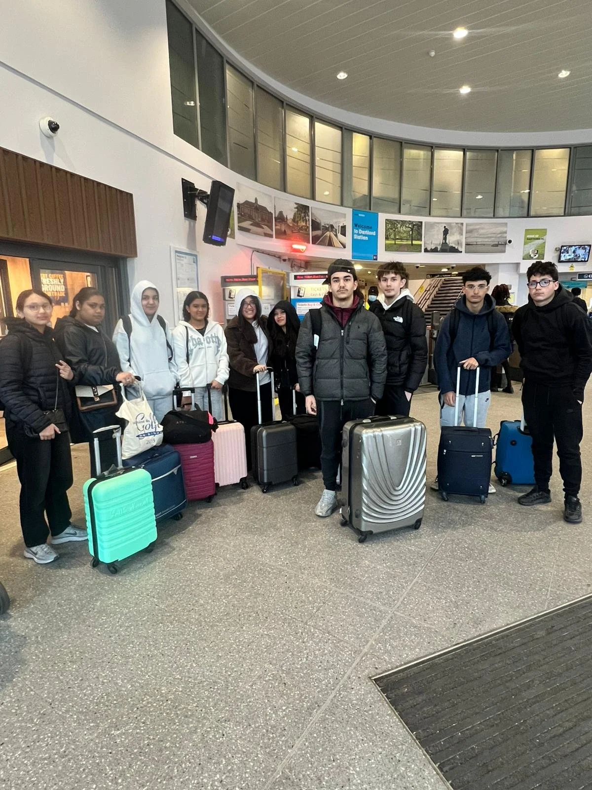 A group of eight young travelers with luggage standing in an airport terminal.