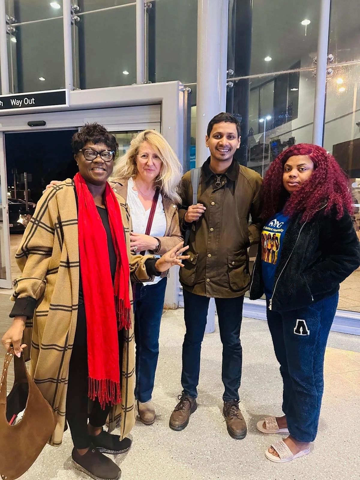 Four women and one man standing outside at night, posing for a photo at an entrance or exit of a building.