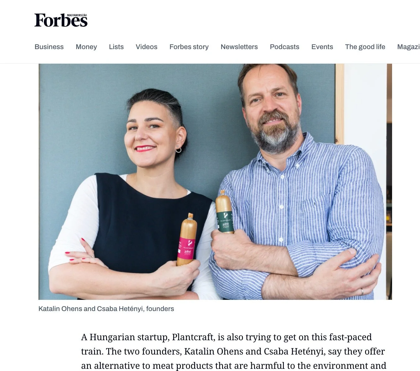 Katalin Ohens and Csaba Hetény, founders of a Hungarian startup, standing against a teal wall, holding plant-based meat products, smiling.