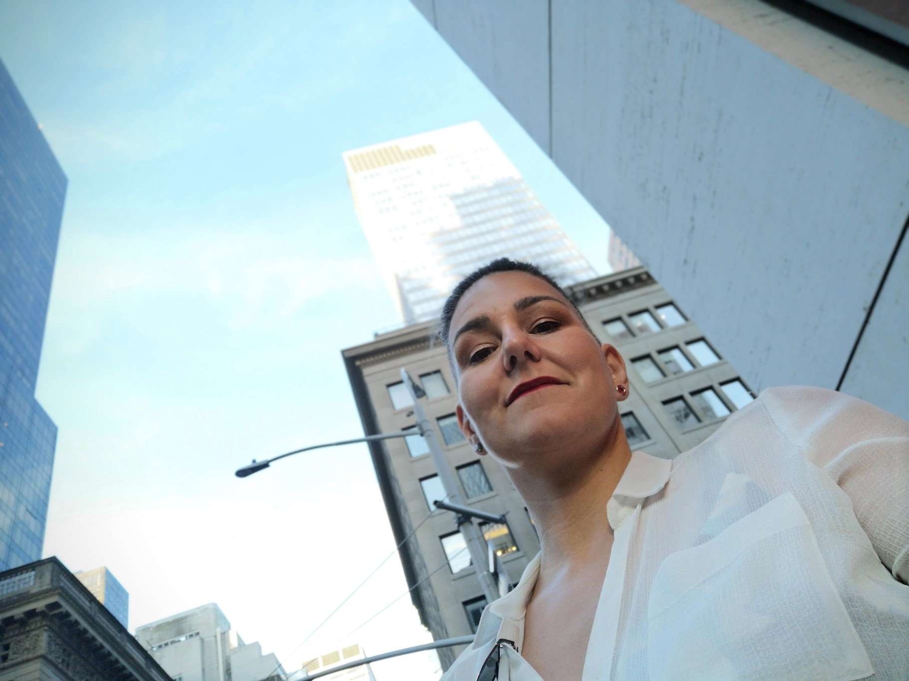 Kati Ohens taking a selfie on a New York street with tall buildings and a clear blue sky in the background.