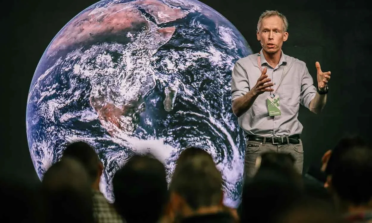 Johan Rockström giving a presentation about planetary boundaries with a large image of Earth behind him to an audience.