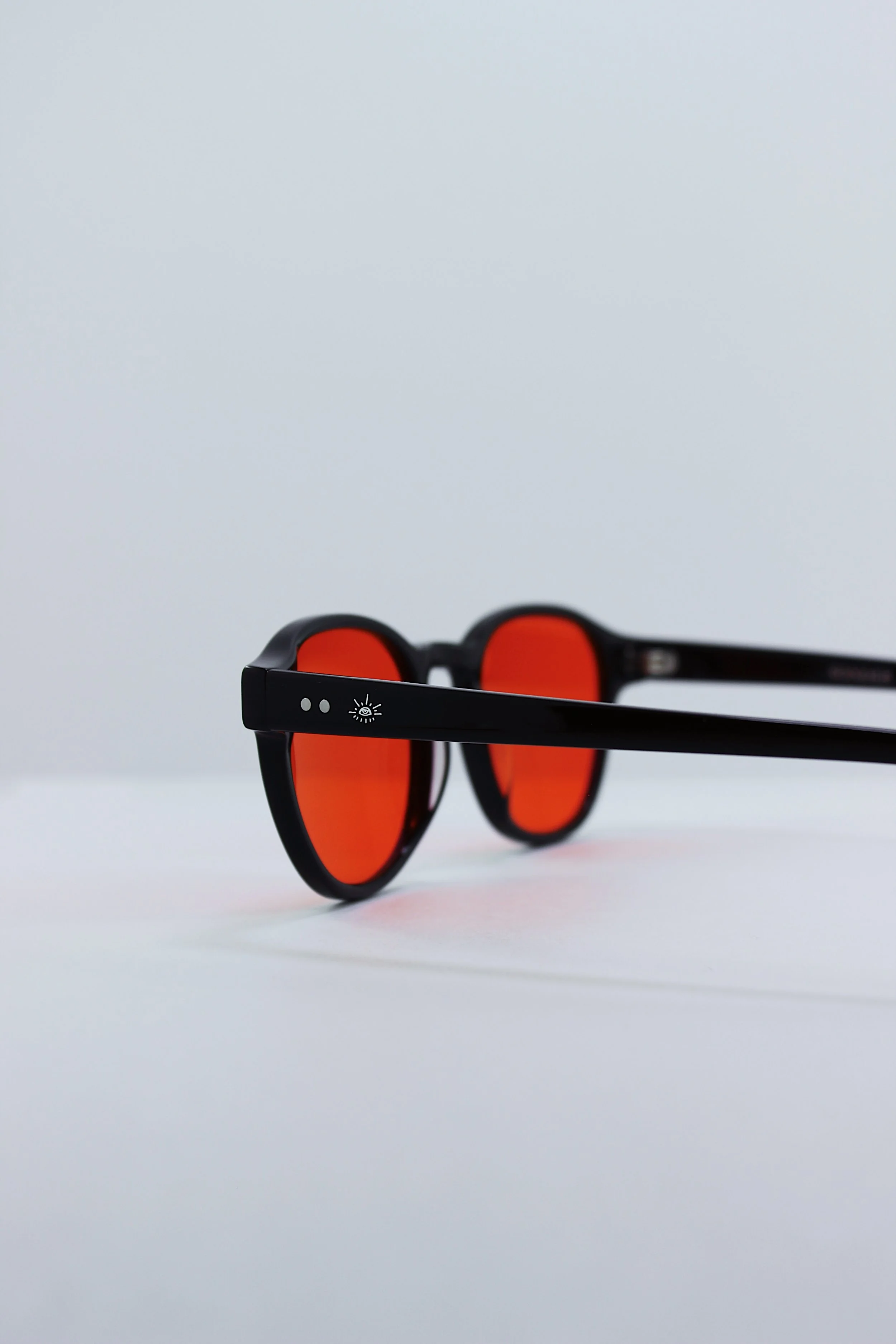 Black blue light eyewear glasses with red lenses on a white surface against a light gray background.