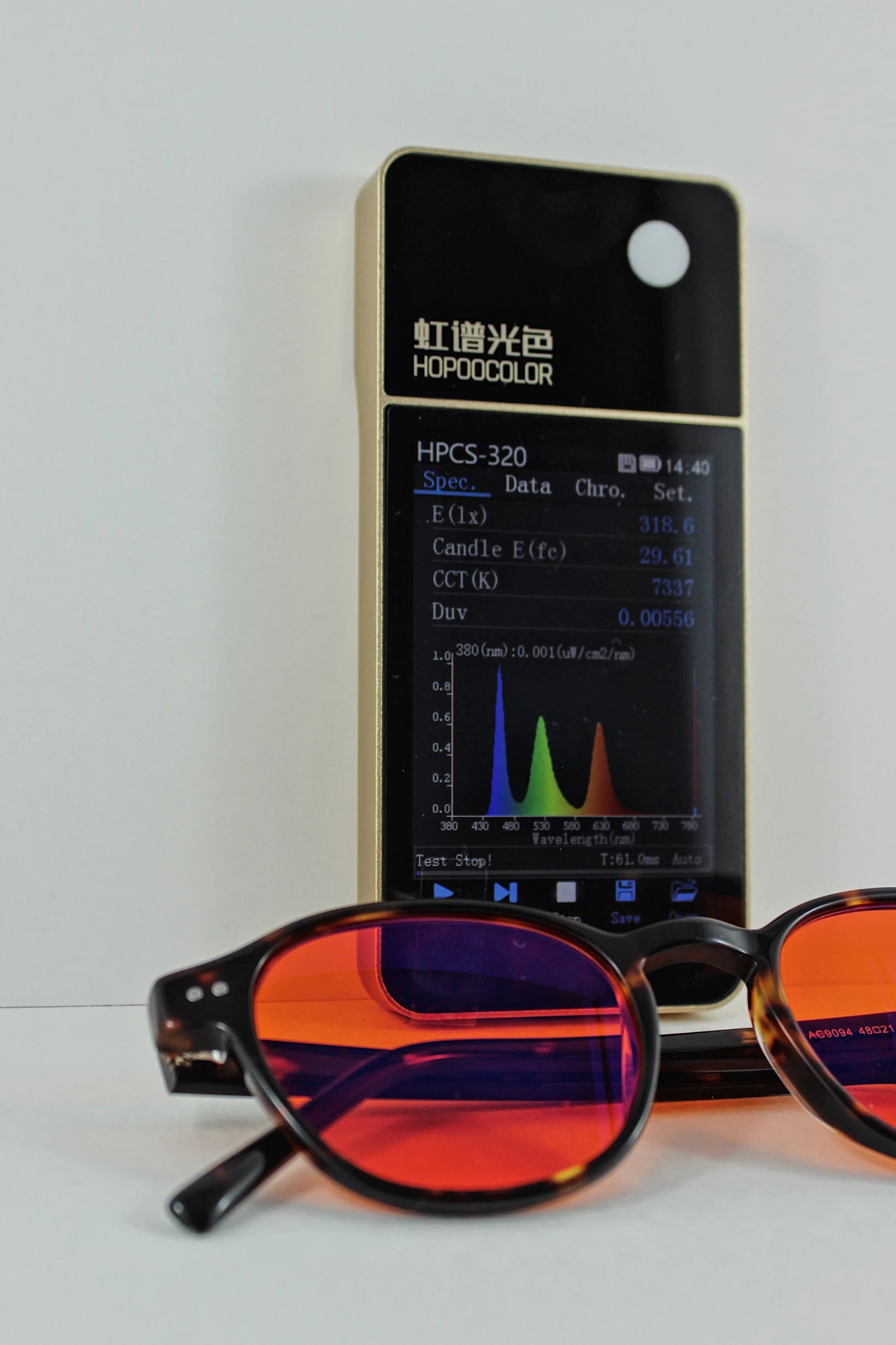 A handheld device displaying spectral analysis data, with sunglasses with tinted frames and lenses in front of it.