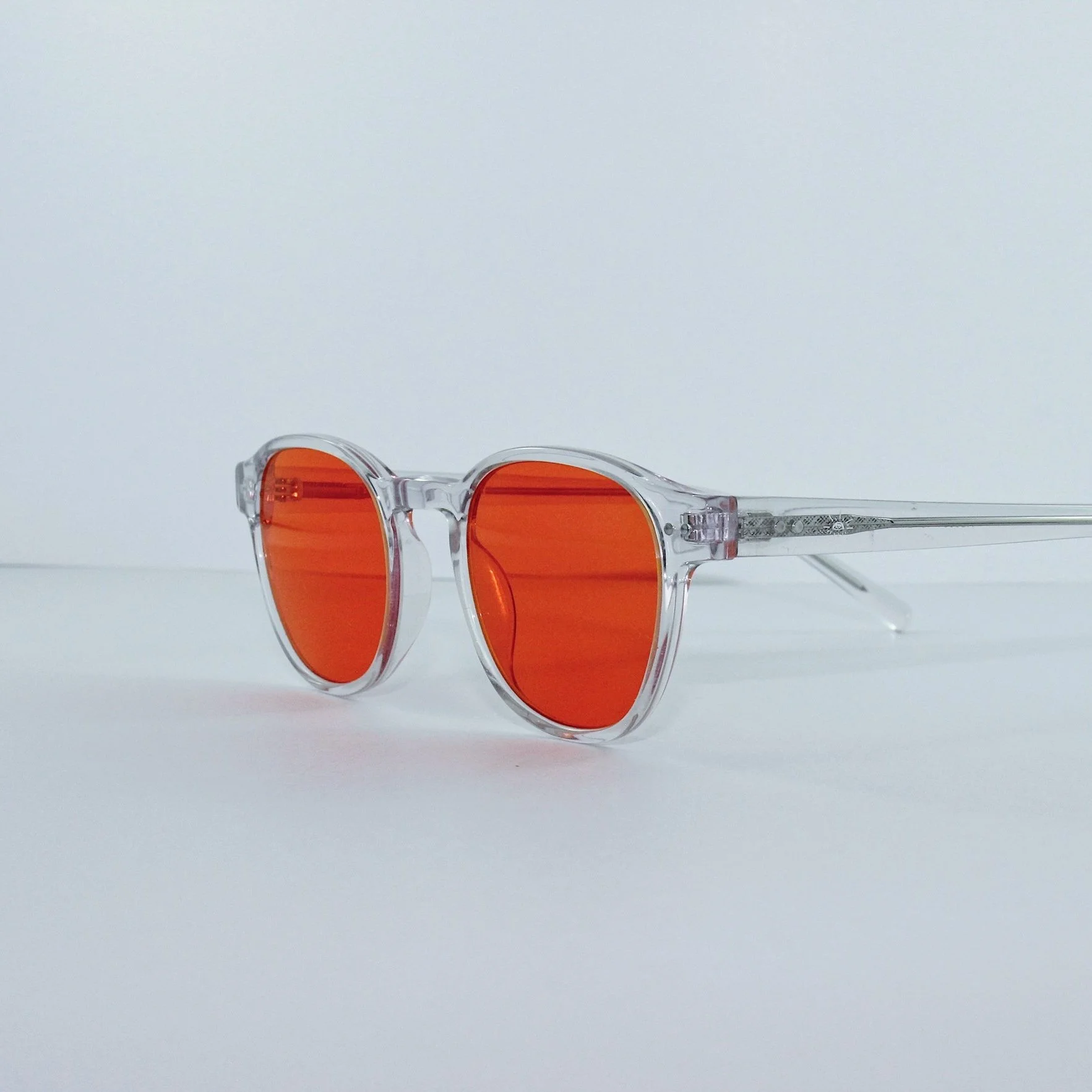 Clear eyewear glasses with orange-tinted lenses on a white surface