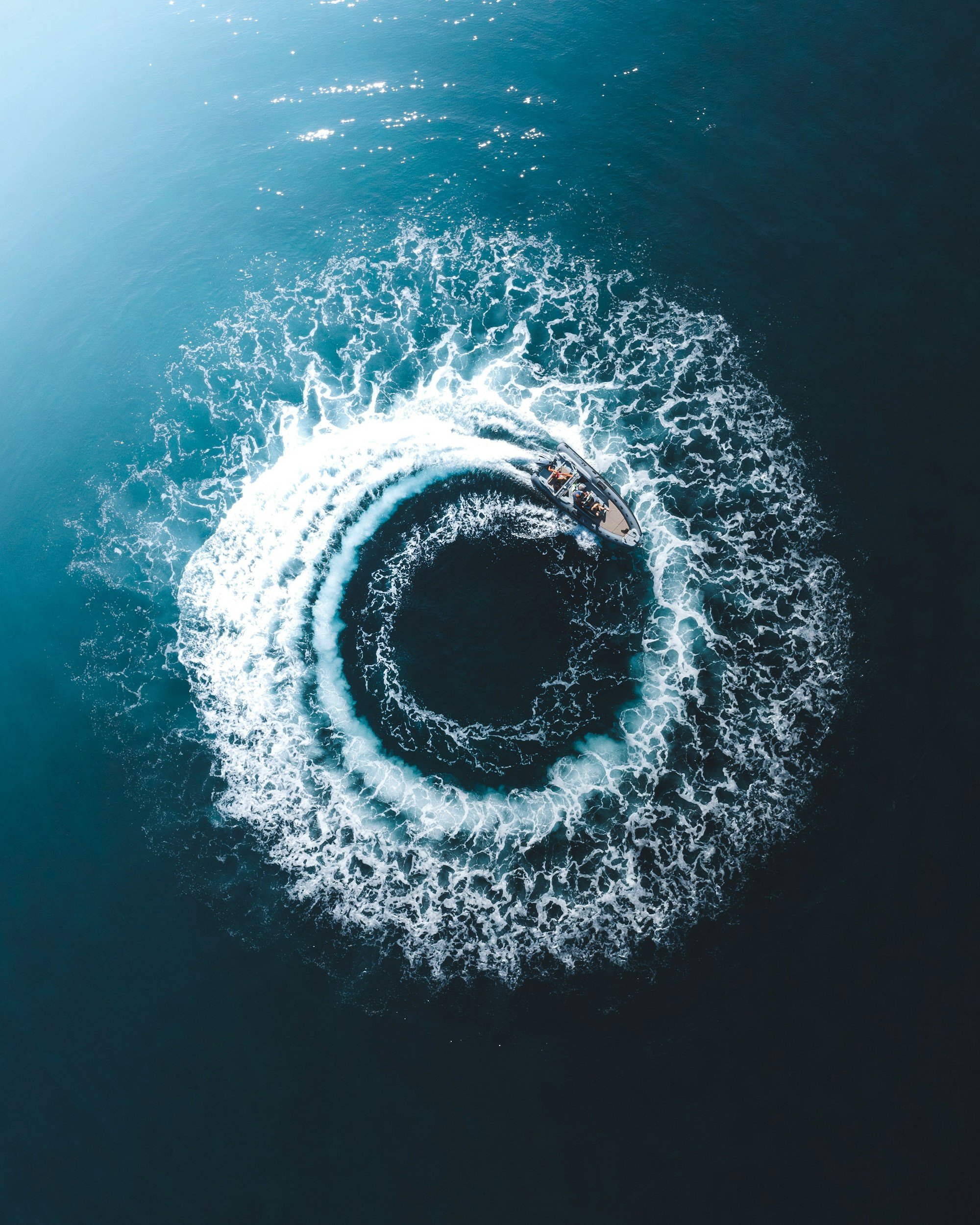 An aerial view of a speedboat moving across the open water, creating a white foamy trail behind it in a deep blue ocean.