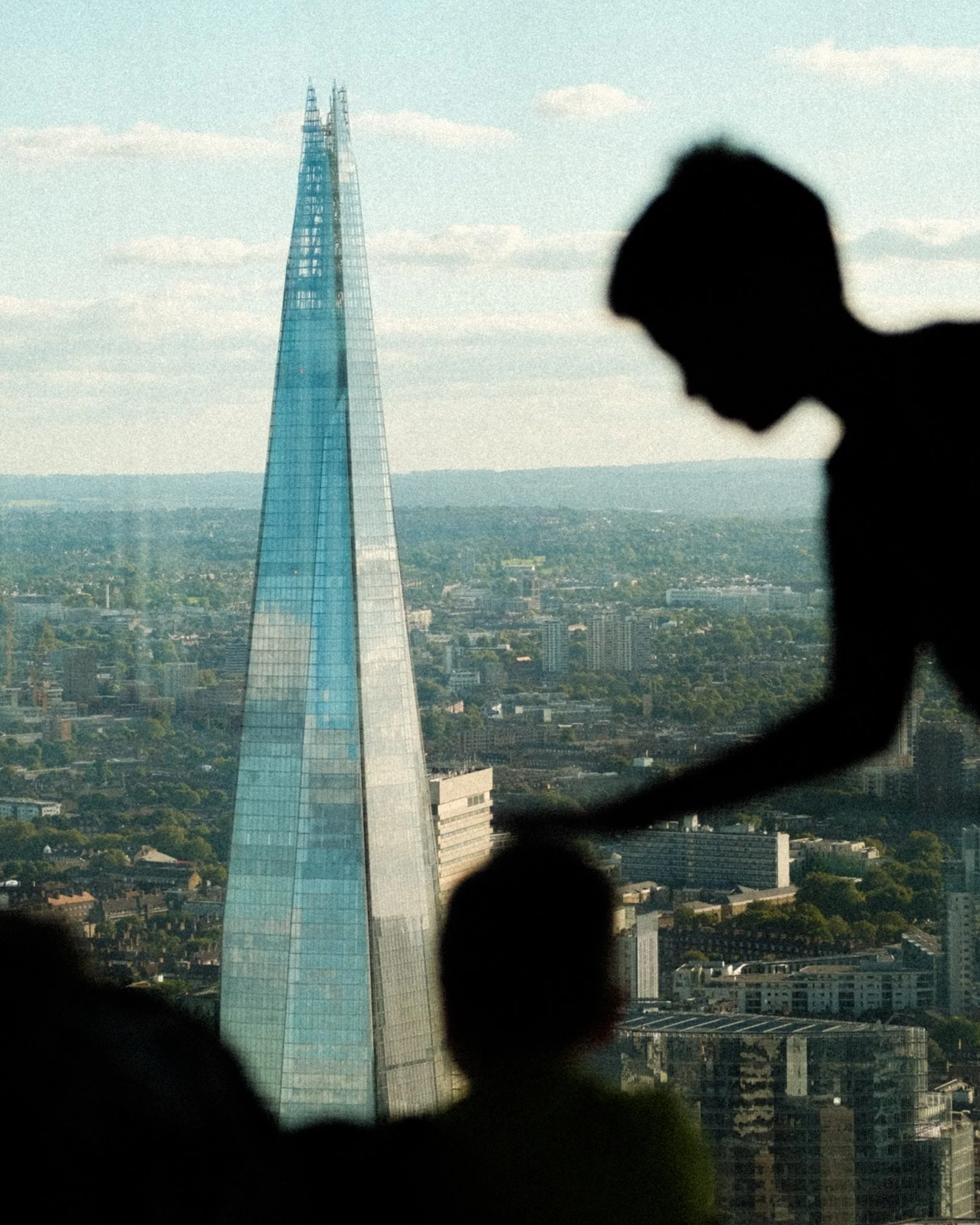 A skyline view of London featuring The Shard, a tall glass skyscraper, with a silhouette of a person's head and shoulders in the foreground.