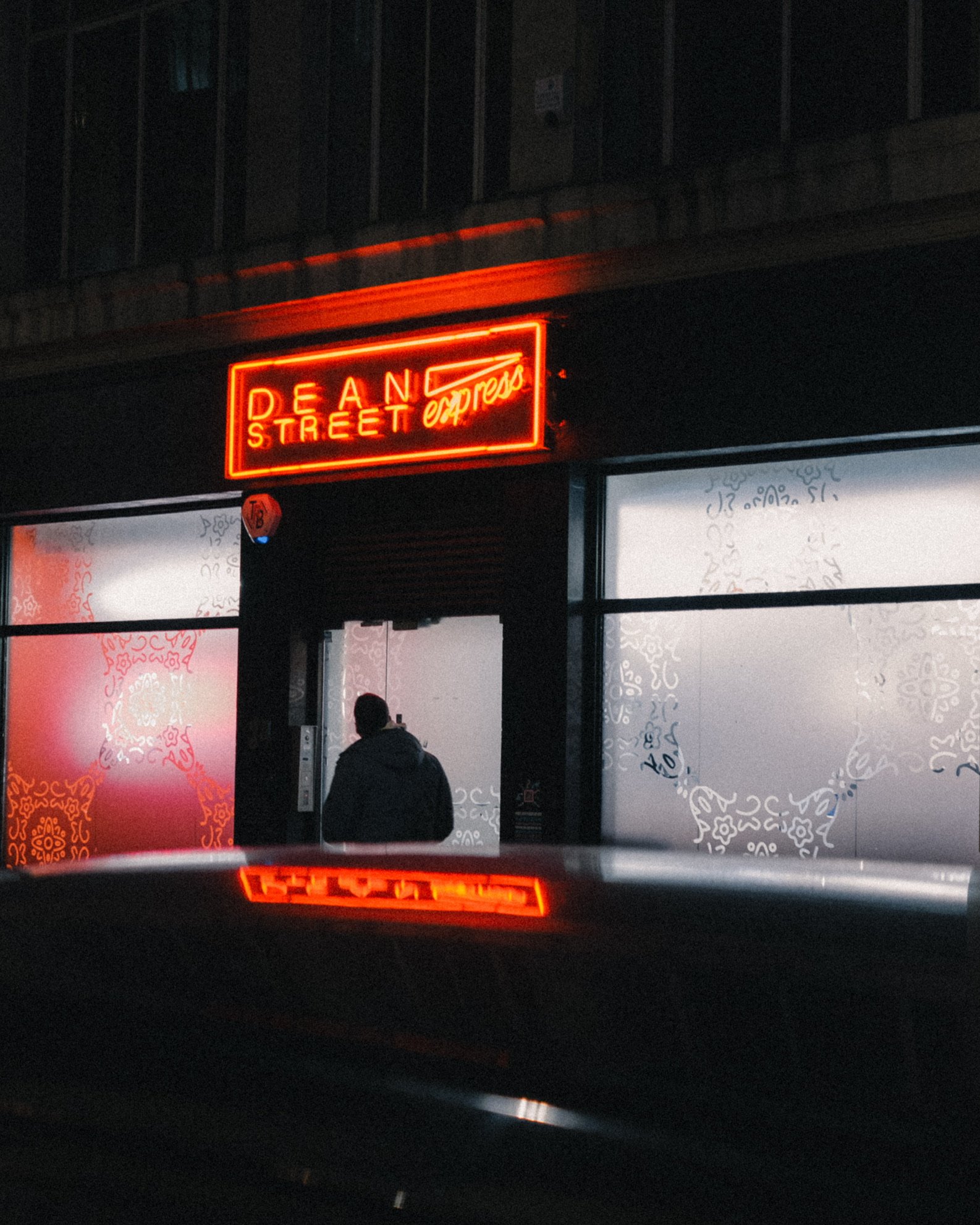 A neon sign that reads 'DANCE STREET express' hanging above a storefront at night, with a person standing in front of the window under the sign.