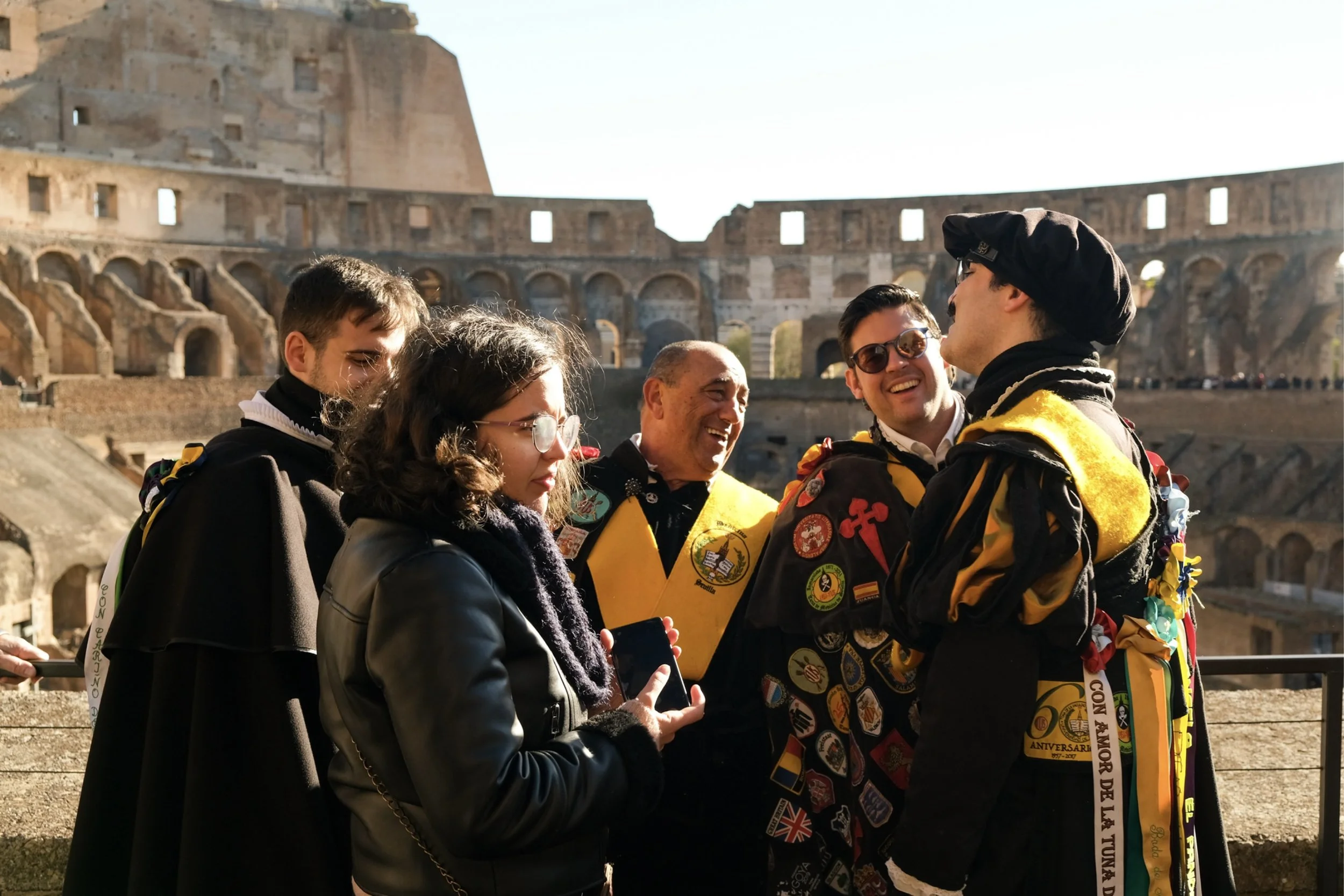 A group of multicultural tourists in front of the Colosseum in Rome, Italy, dressed in casual clothes, some wearing sunglasses and scarves, smiling and preparing for a tour.