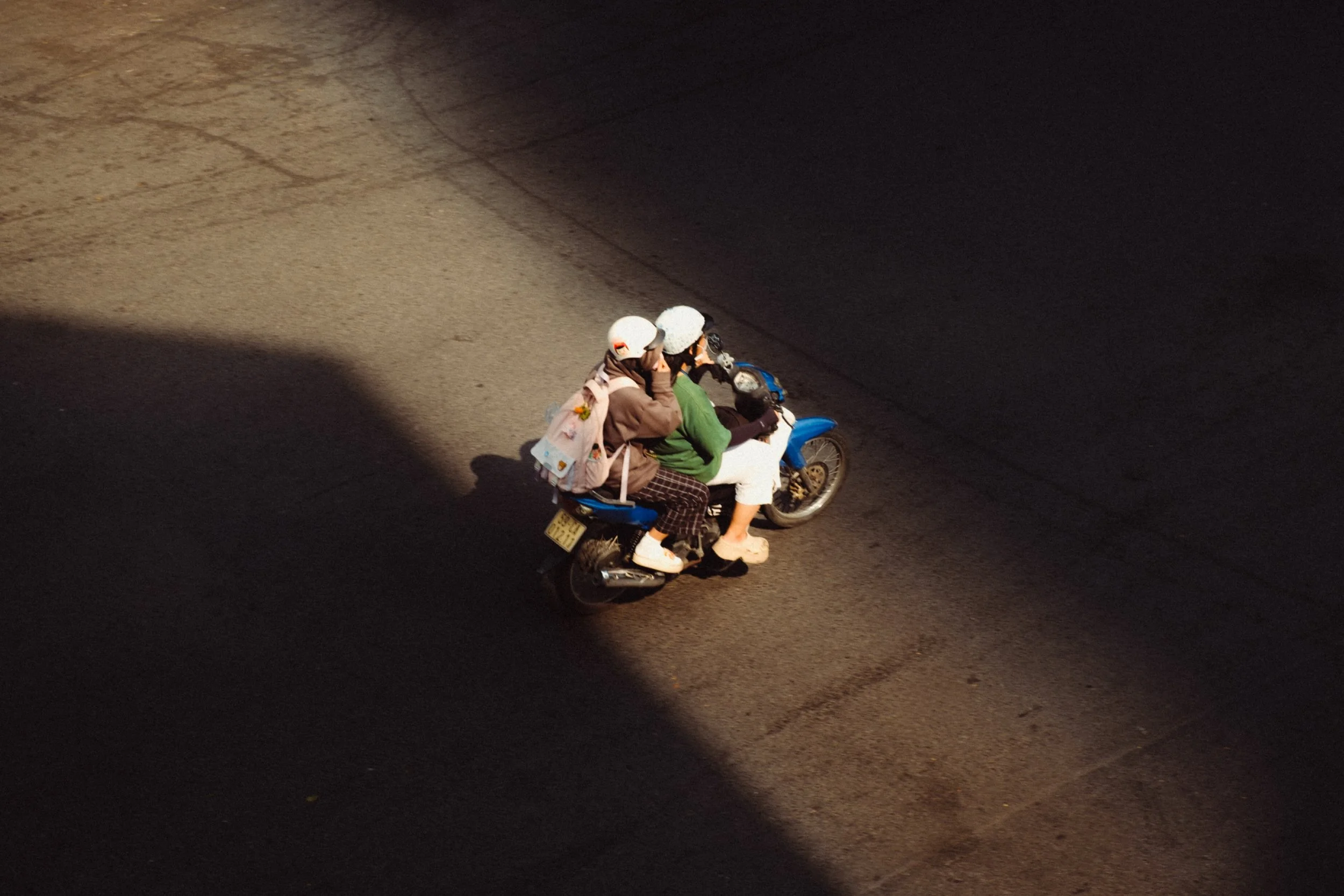 Two people riding a blue motorcycle on a dark street at night, one wearing a white helmet and the other wearing a black helmet.