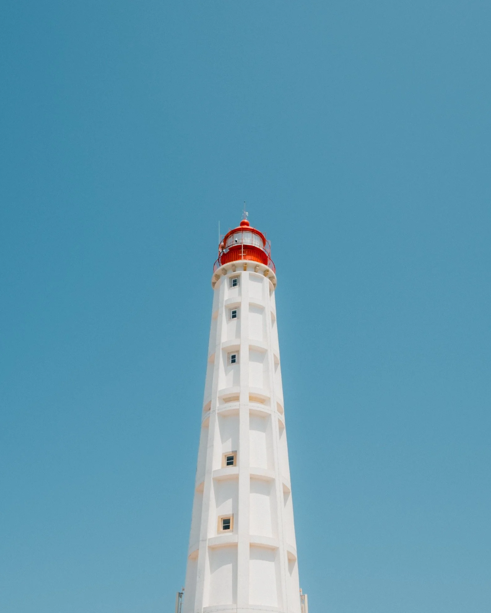 A tall white lighthouse with a red top against a clear blue sky.