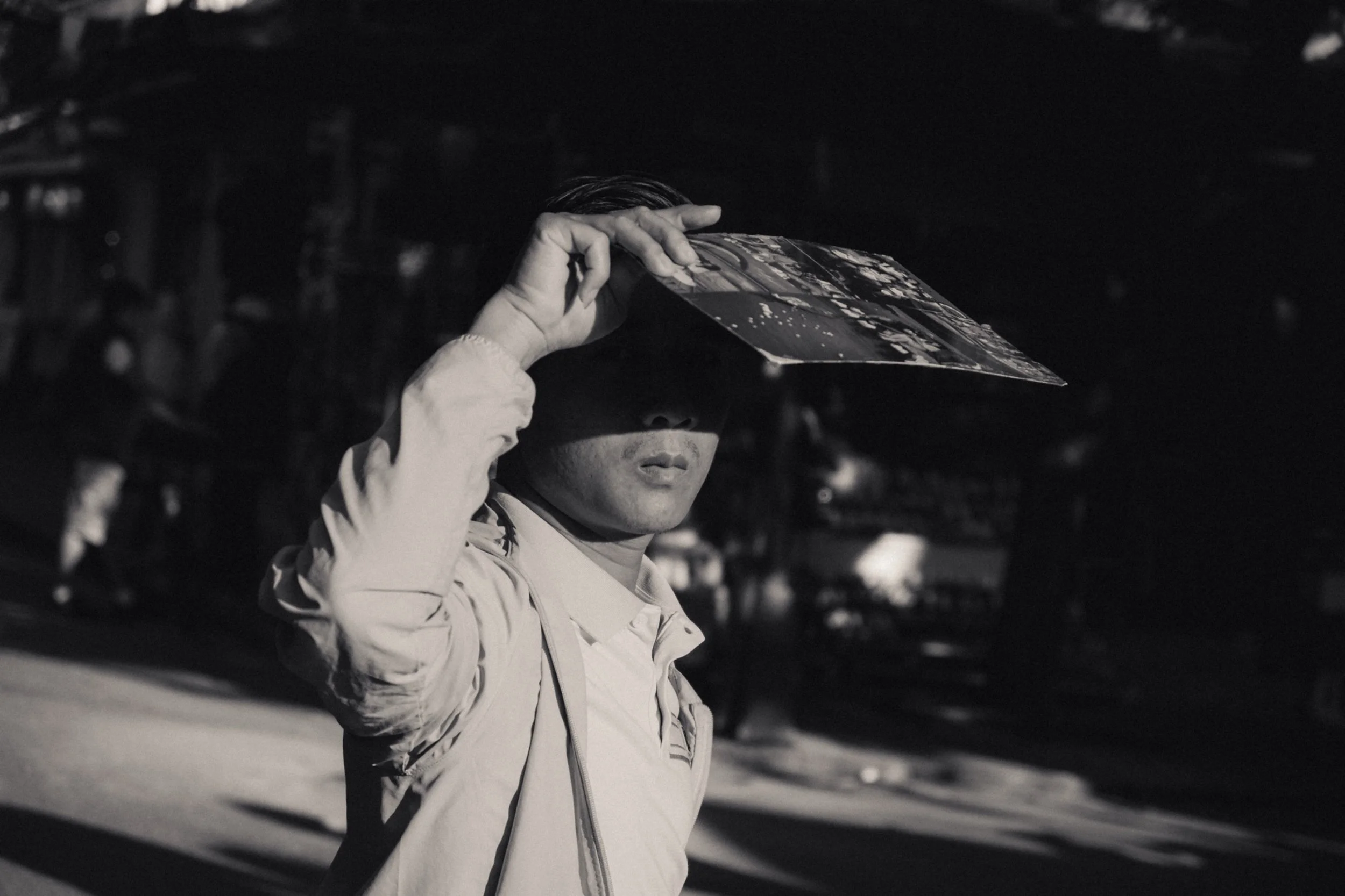 A person holding a photo above their head, partially covering their face, outdoors at night.