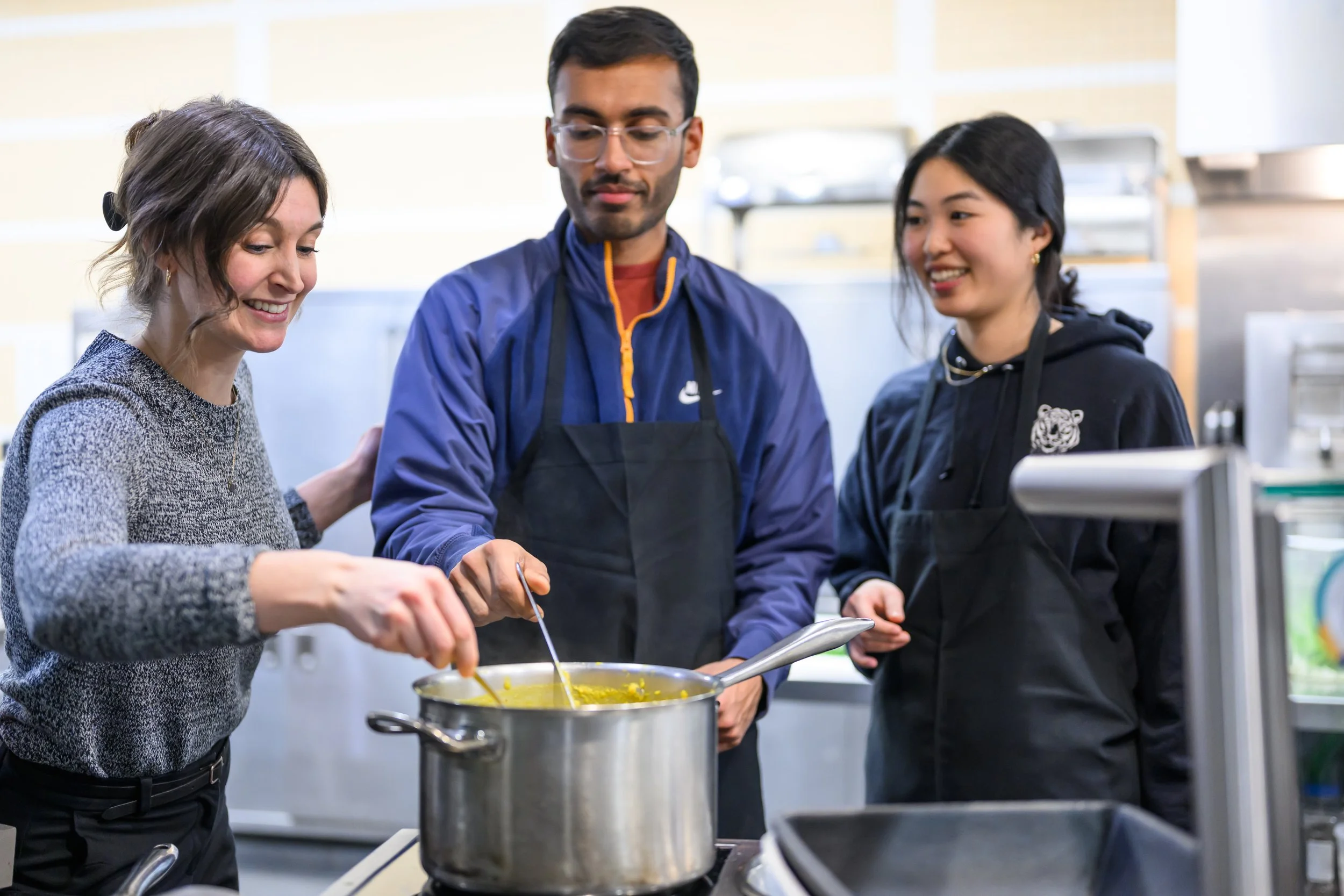 Three people standing over a pot cooking together.
