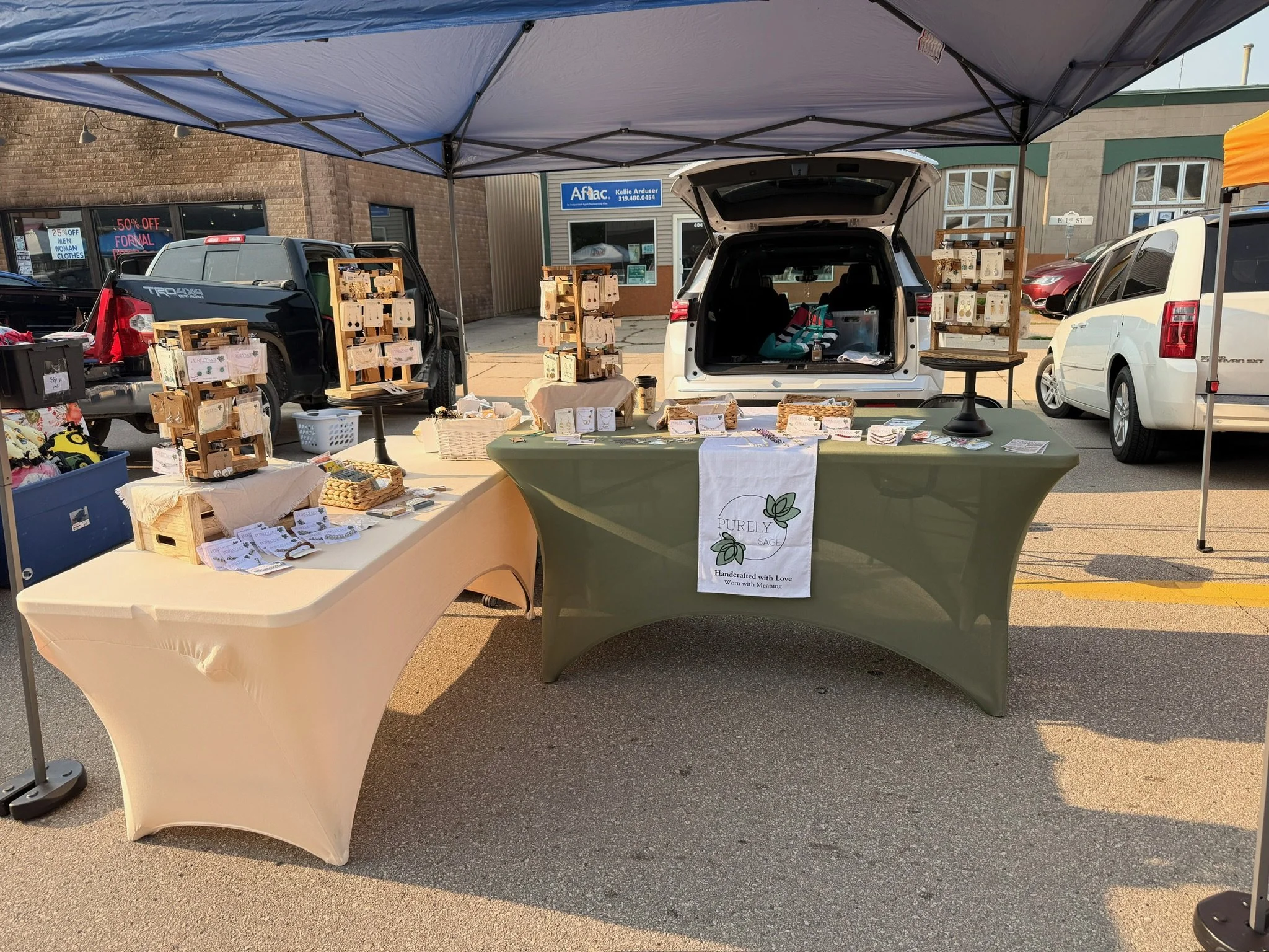 Outdoor market stall set up under a canopy with tables displaying jewelry and crafts
