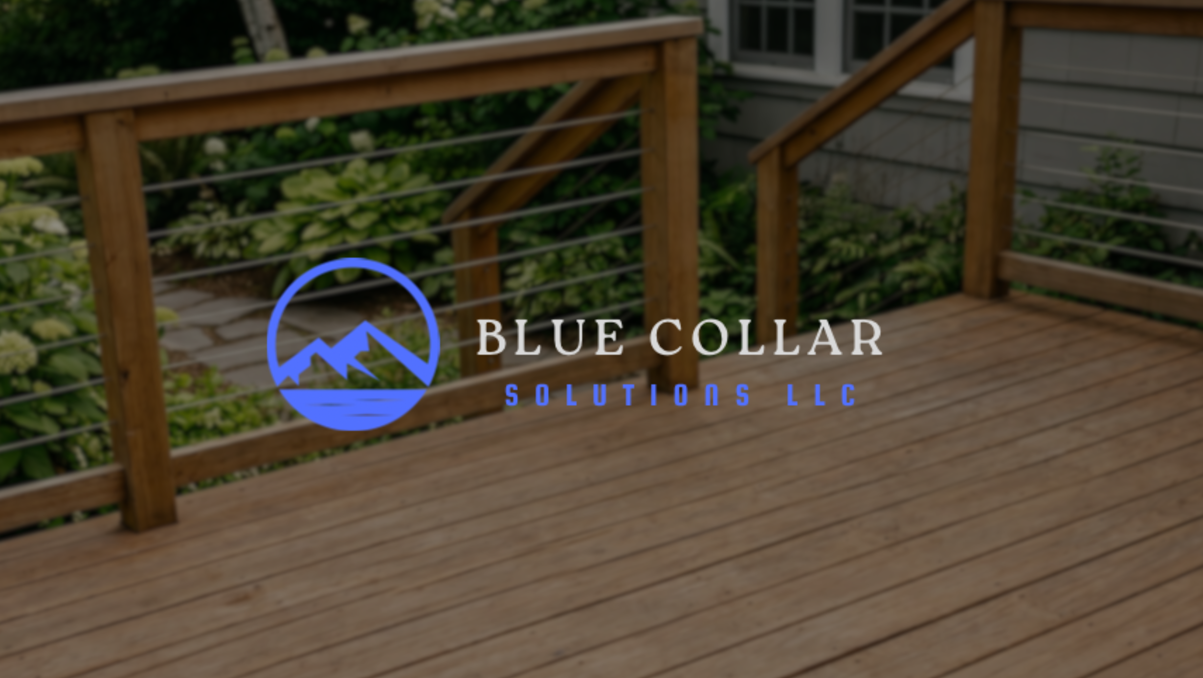 A wood deck with a railing, with green bushes and a house in the background. The image has a blue and white logo for Blue Collar Solutions LLC overlayed on it.