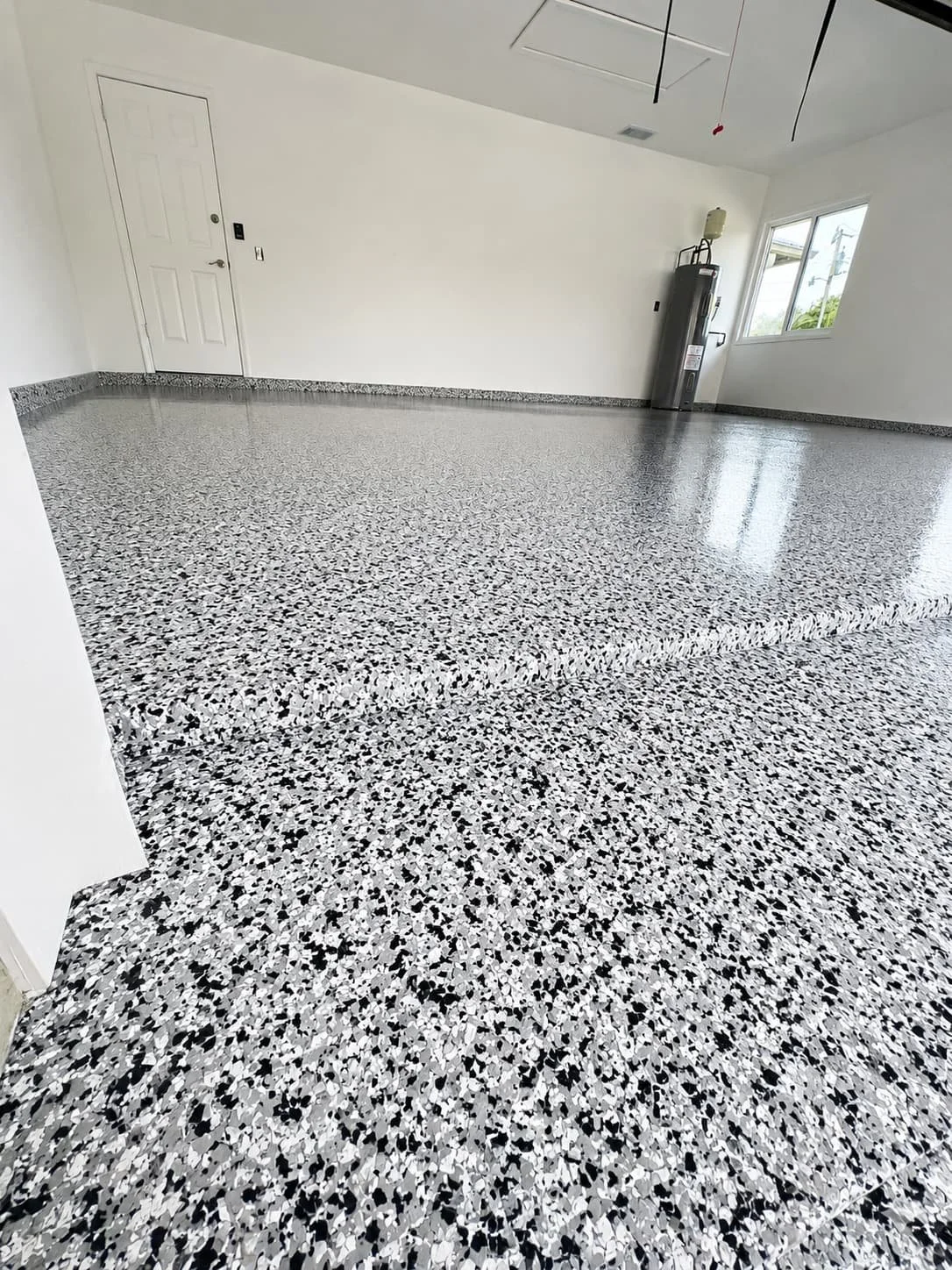 Empty room with flake epoxy flooring, white walls, window, and water heater in corner.