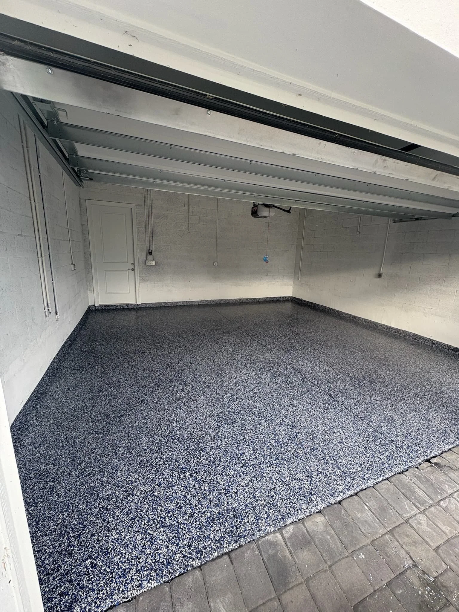 Empty garage with a speckled epoxy floor coating, white brick walls, and an open garage door.