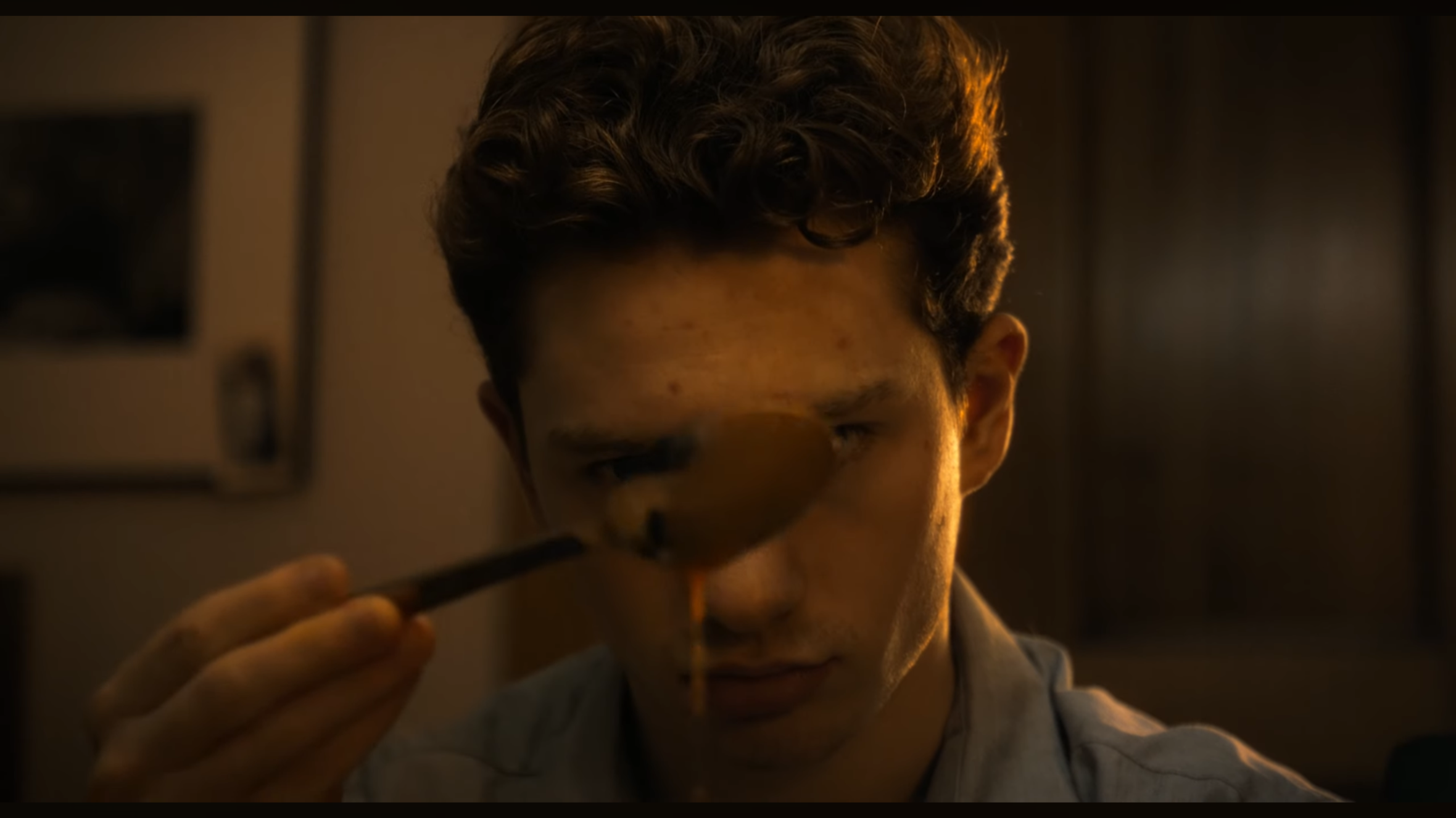 A young man with curly hair is using a magnifying glass to examine a small object.