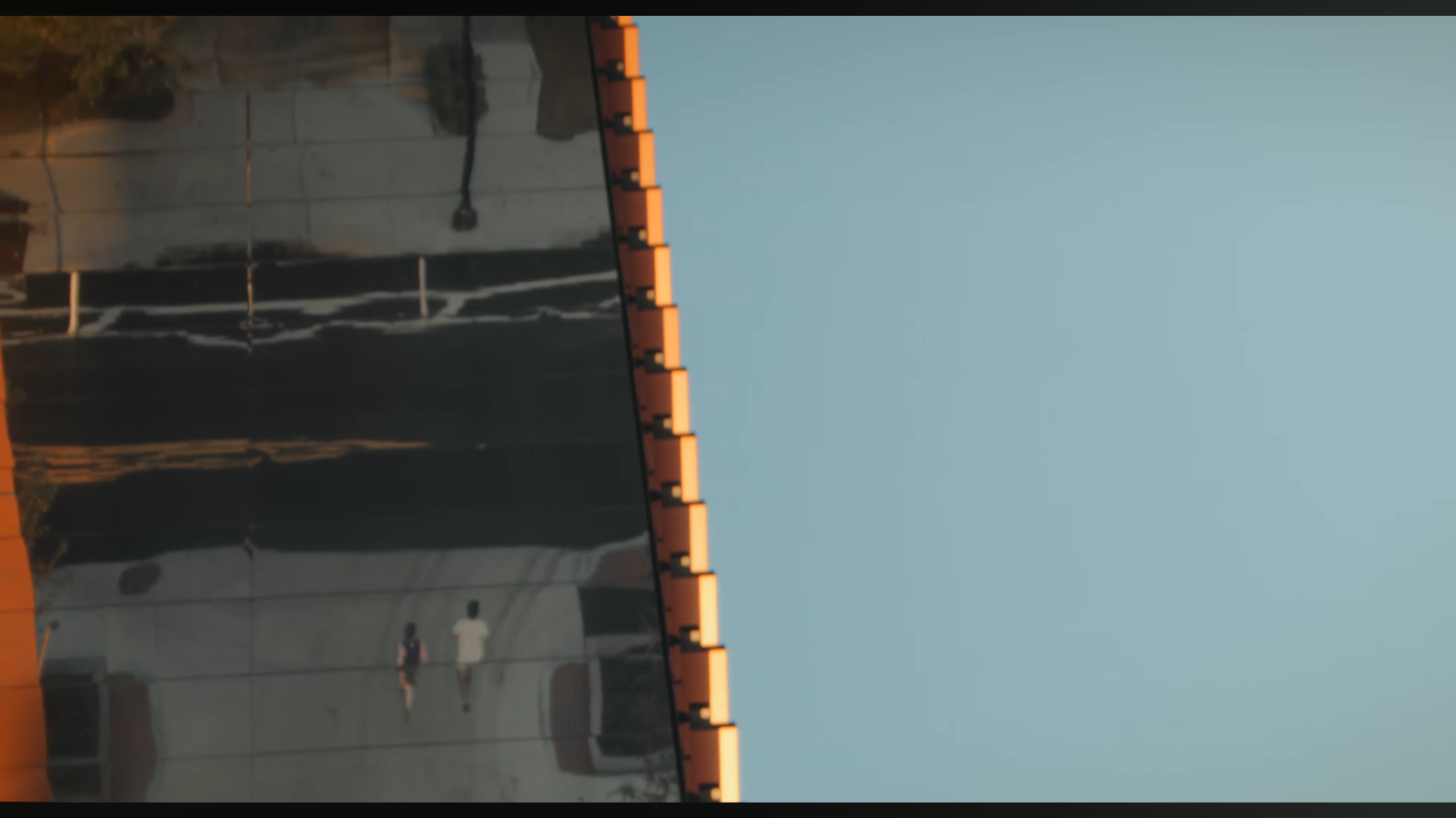 Reflection of a building with orange rooftop of a modern glass structure, two people walking in front, under a clear sky.