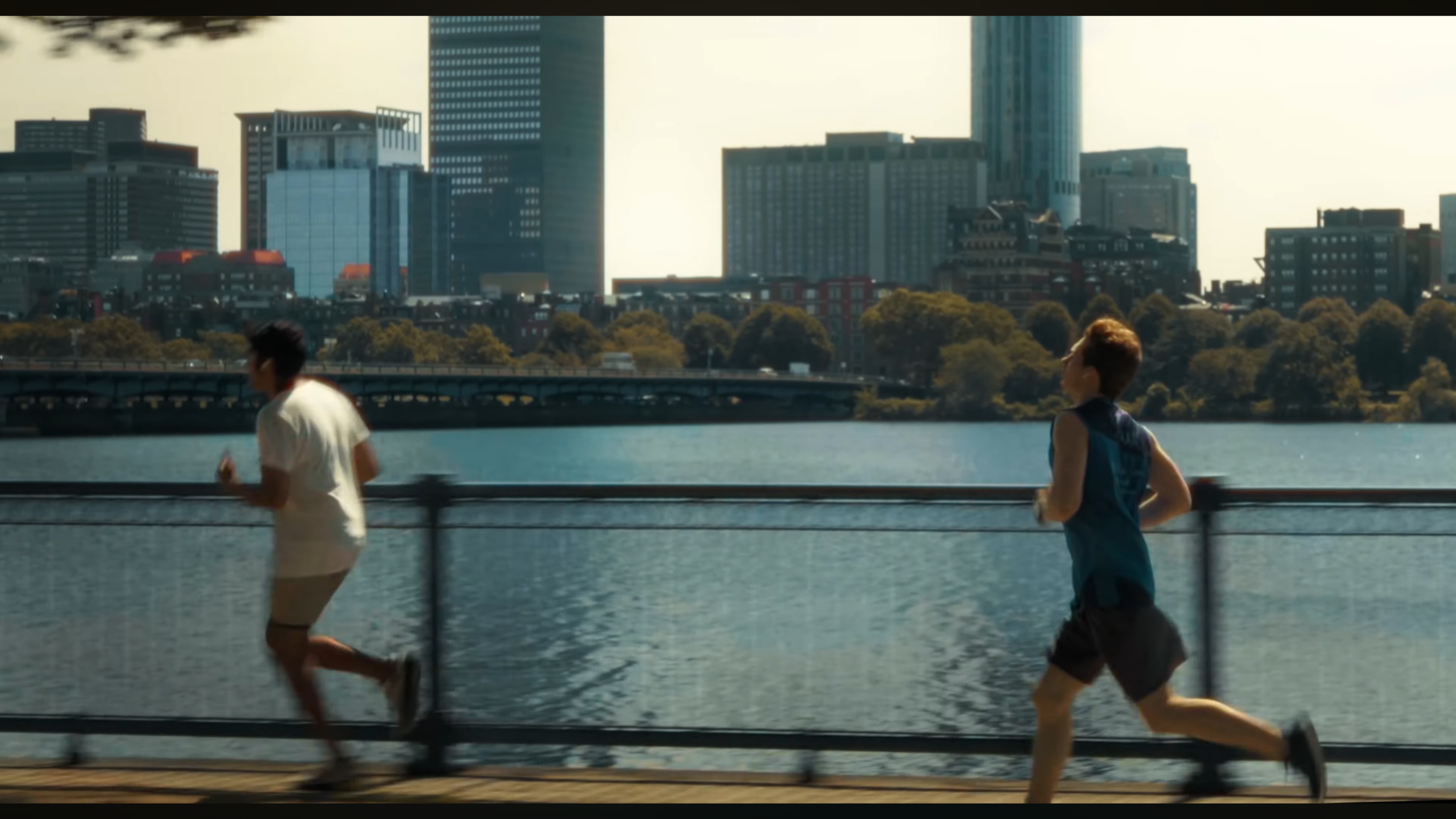 Two people jogging along a waterfront with city skyscrapers in the background.